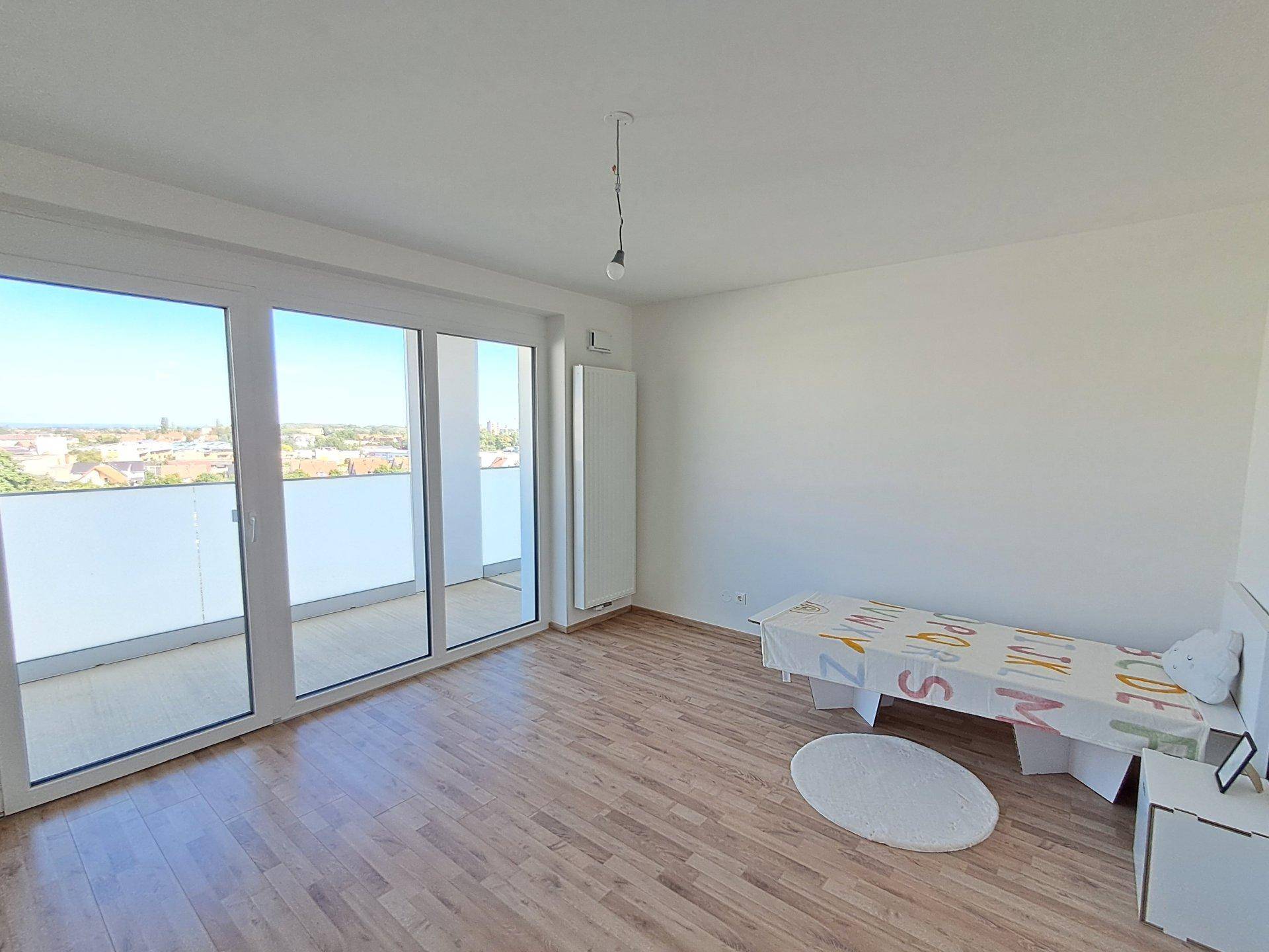 Kinderzimmer mit Laminatboden und großem Fenster, das Zugang zu einem Balkon bietet.