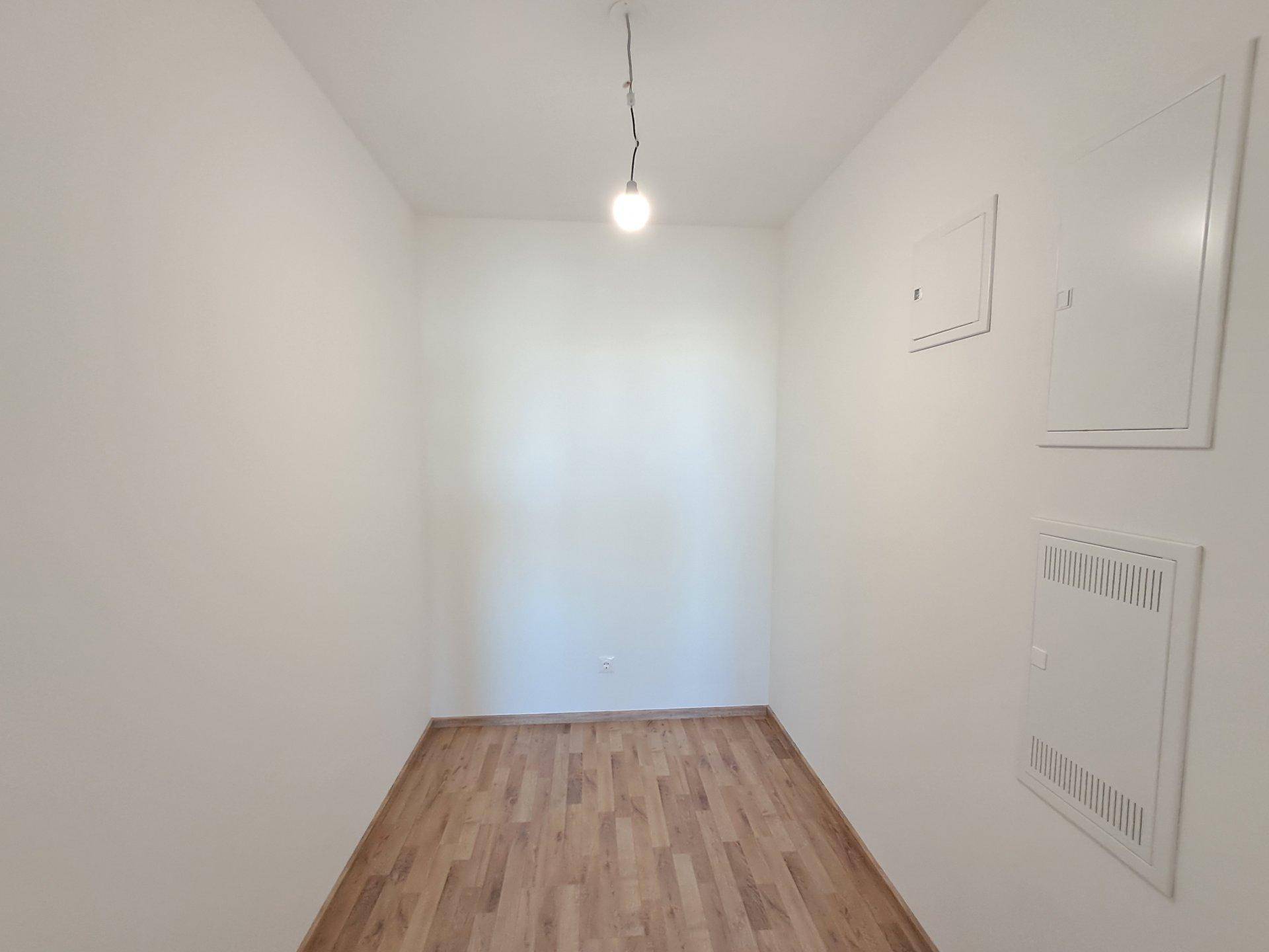 Heller Flur oder Abstellraum mit Laminatboden und weißen Wänden, bereit zur Nutzung.