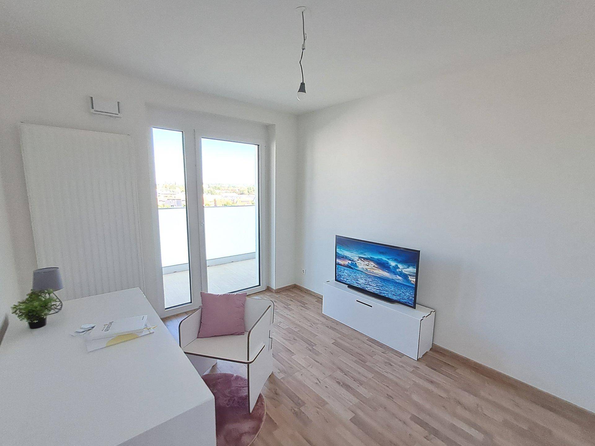 Helles Arbeitszimmer mit Laminatboden und großem Fenster, das viel Tageslicht hereinlässt.