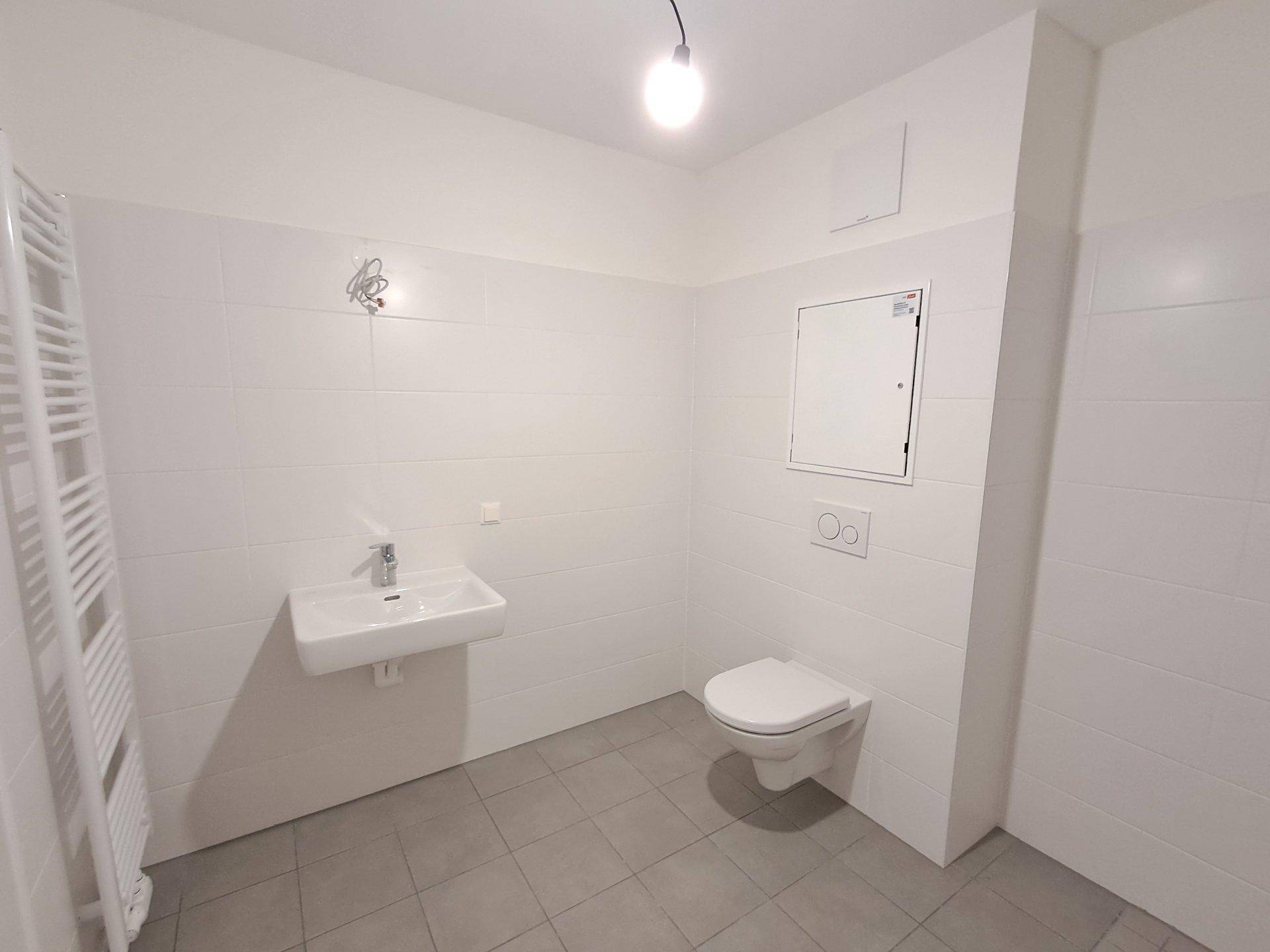 Funktionales Badezimmer mit Waschbecken, Wand-WC und beheiztem Handtuchhalter.