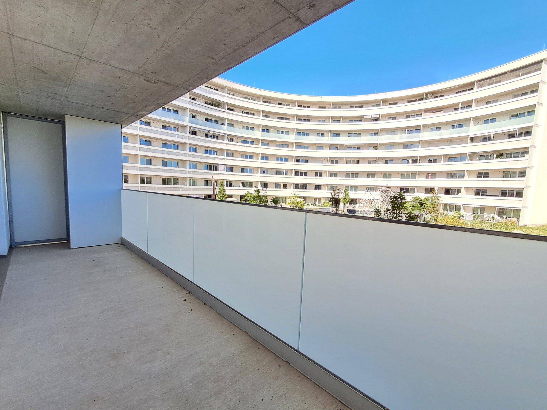 Balkon mit Blick auf eine moderne Wohnanlage und blauen Himmel.