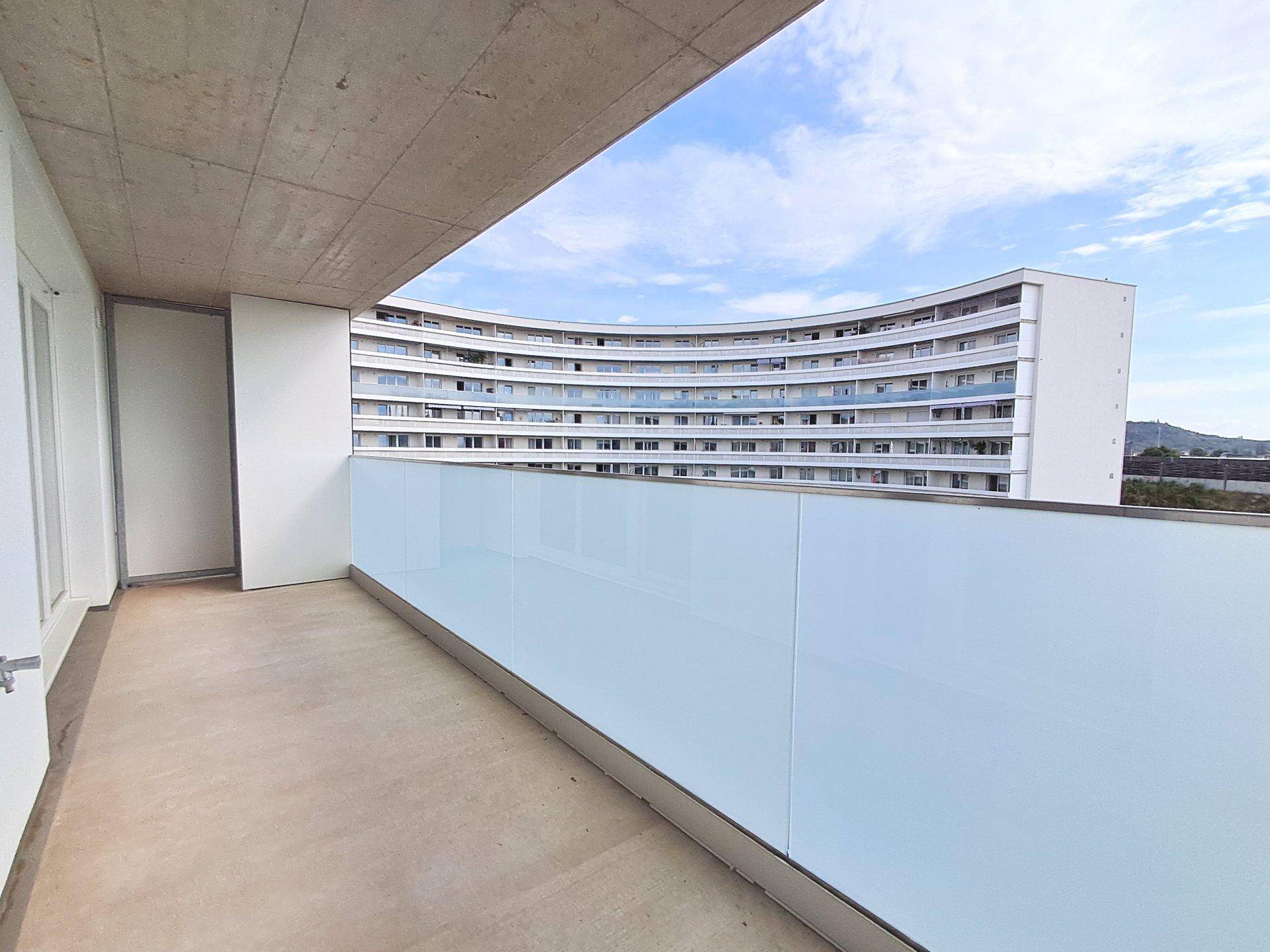 Geräumiger Balkon mit Glasbrüstung und Blick auf die umliegende moderne Architektur.