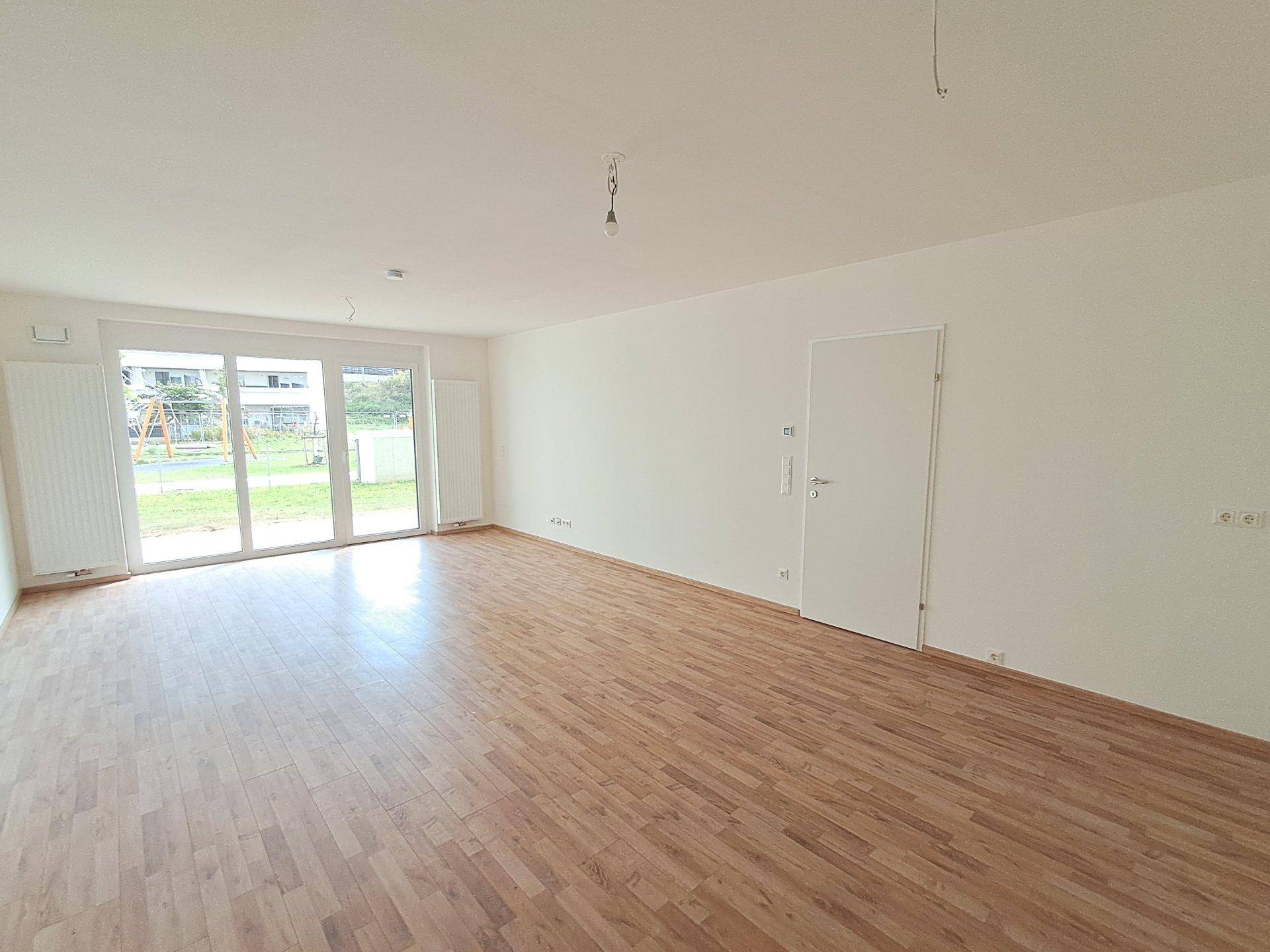 Helles Wohnzimmer mit großen Fenstern und Blick auf den Spielplatz im Außenbereich.
