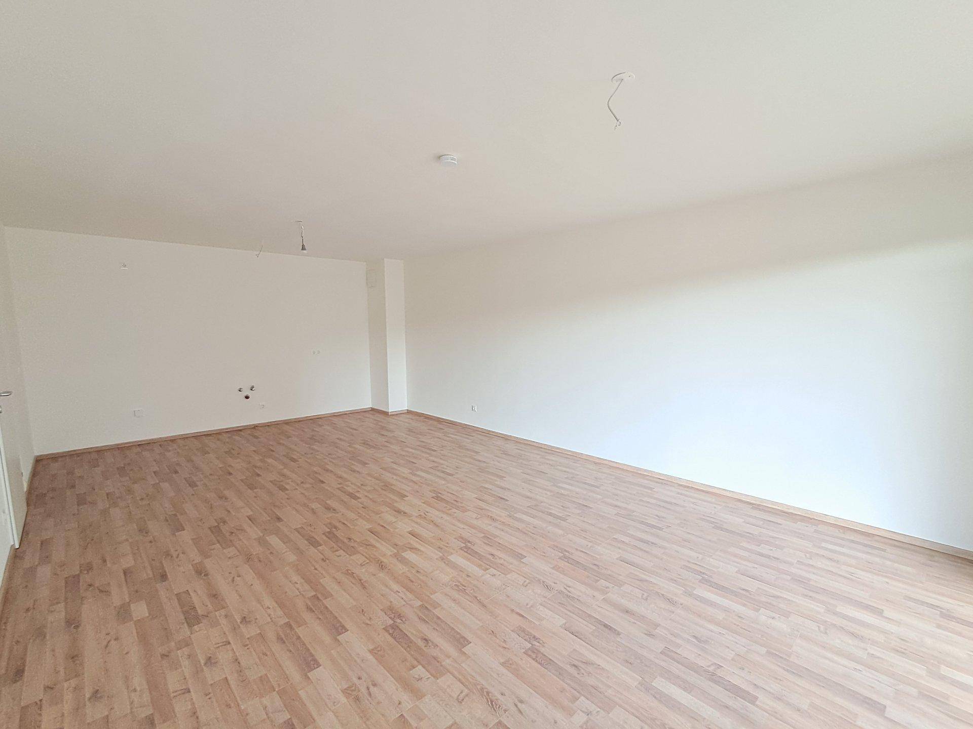 Geräumiges, leeres Wohnzimmer mit hellem Laminatboden und weißen Wänden, bereit zur Einrichtung.