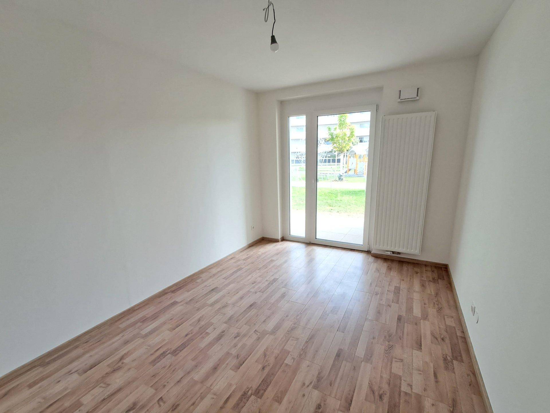 Leeres Zimmer mit Laminatboden und Fenster, das vielseitig genutzt werden kann.
