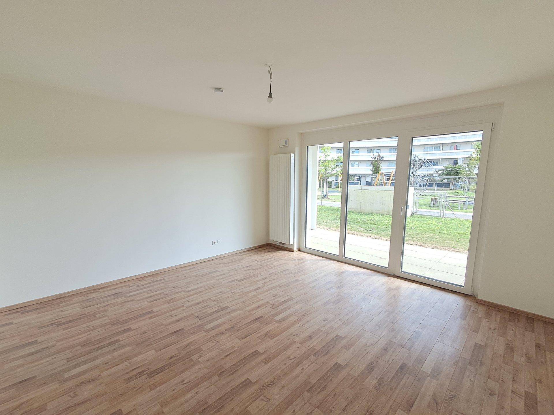 Geräumiges Zimmer mit Laminatboden und breiter Fensterfront zum Außenbereich mit Spielplatz.