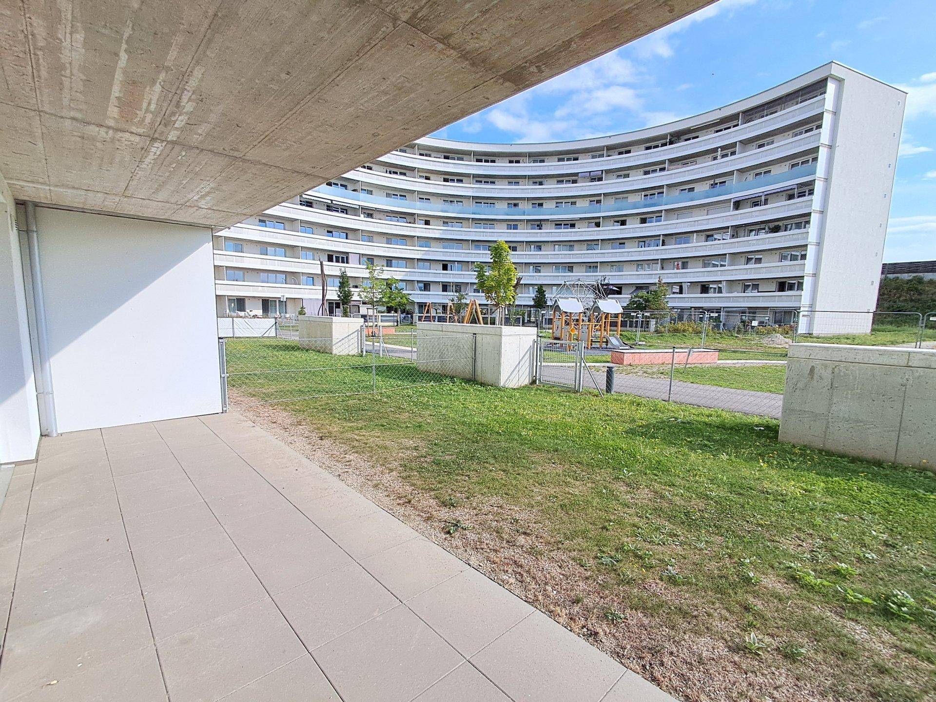 Außenbereich mit gepflasterter Terrasse und Blick auf einen Spielplatz im Hintergrund.