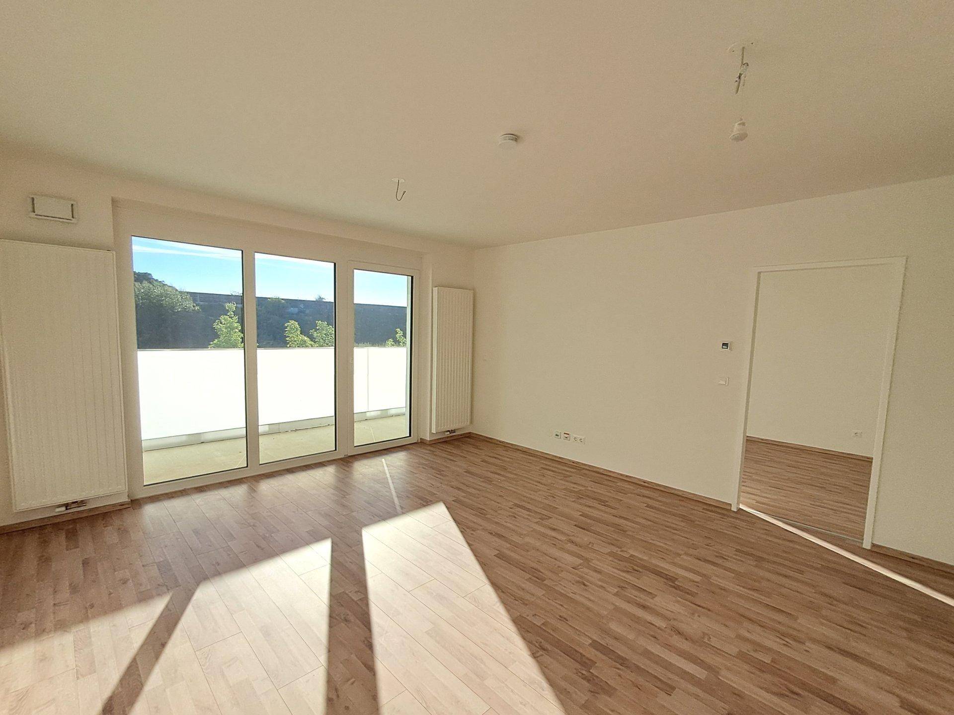 Lichtdurchfluteter Wohnbereich mit Laminatboden und breiter Fensterfront zum Außenbereich.