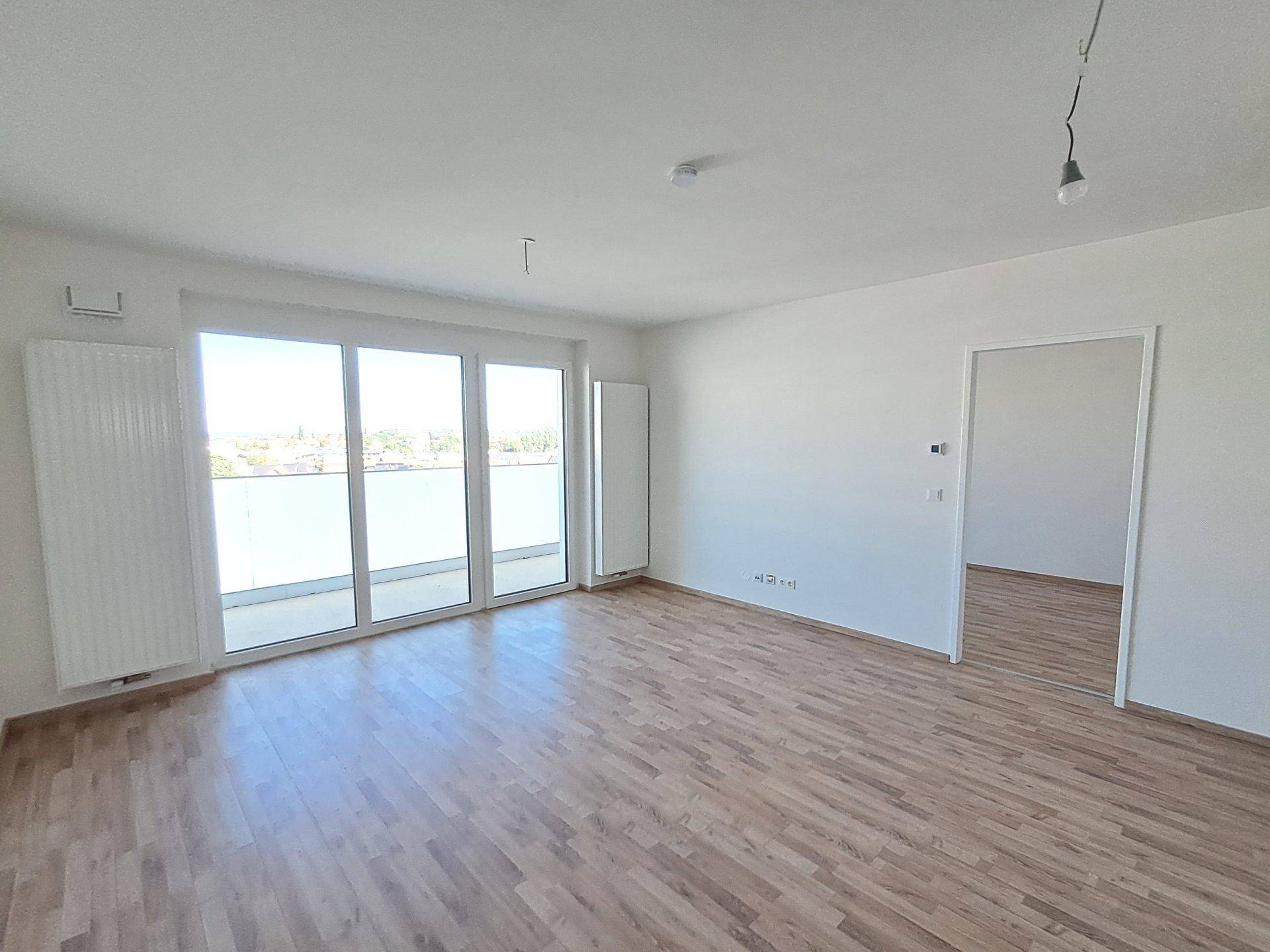 Lichtdurchfluteter Raum mit Holzfußboden und großen Fenstertüren, die zu einem Außenbereich führen.
