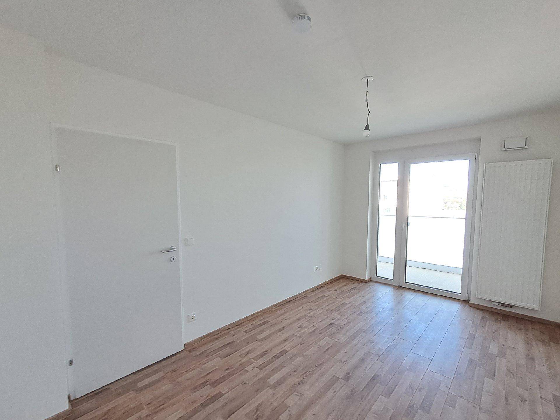 Helles, unmöbliertes Schlafzimmer mit Laminatboden und Zugang zu einem Balkon.