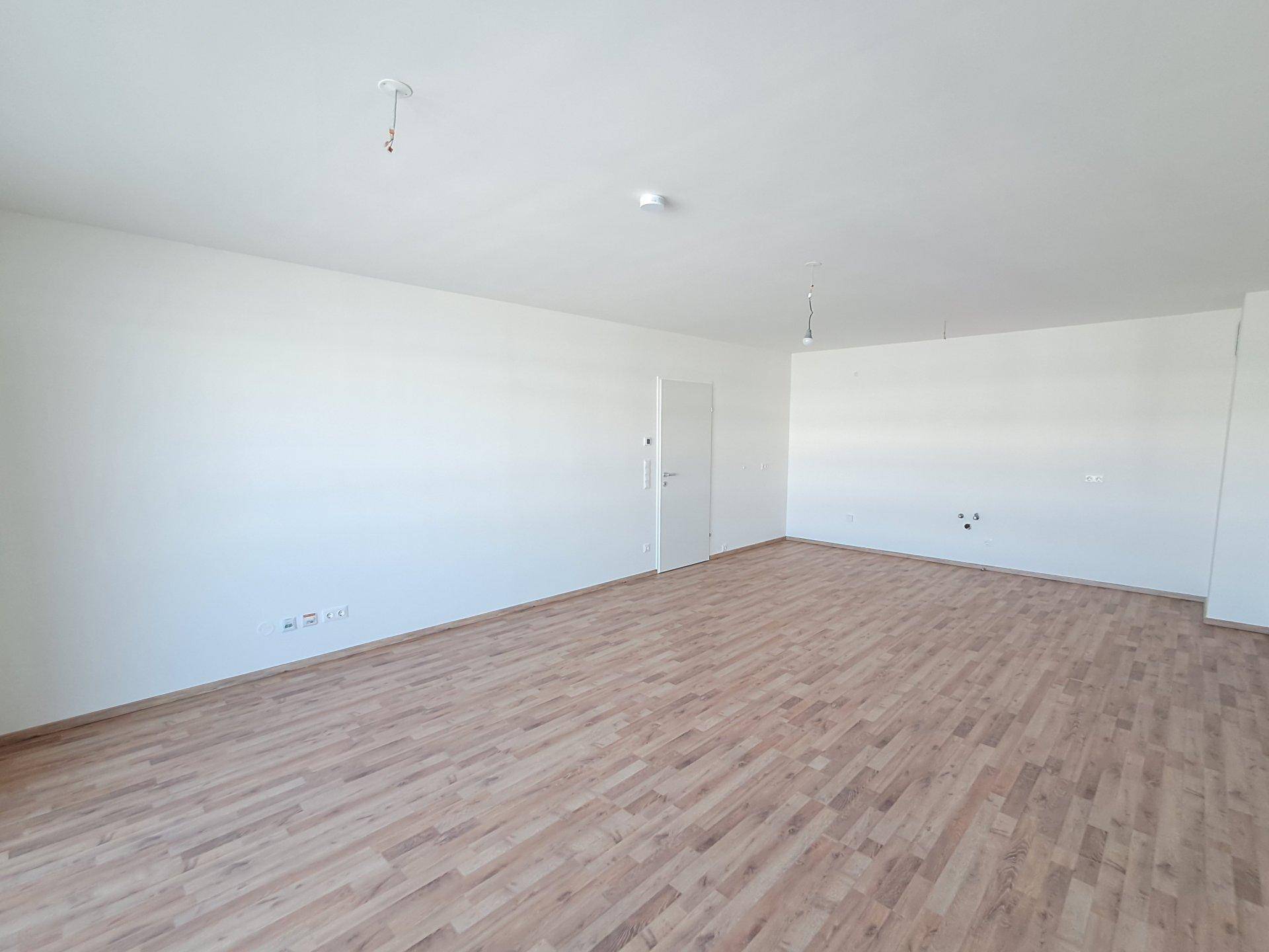 Helles, leeres Wohnzimmer mit Laminatboden und weißen Wänden, bereit zur individuellen Gestaltung.