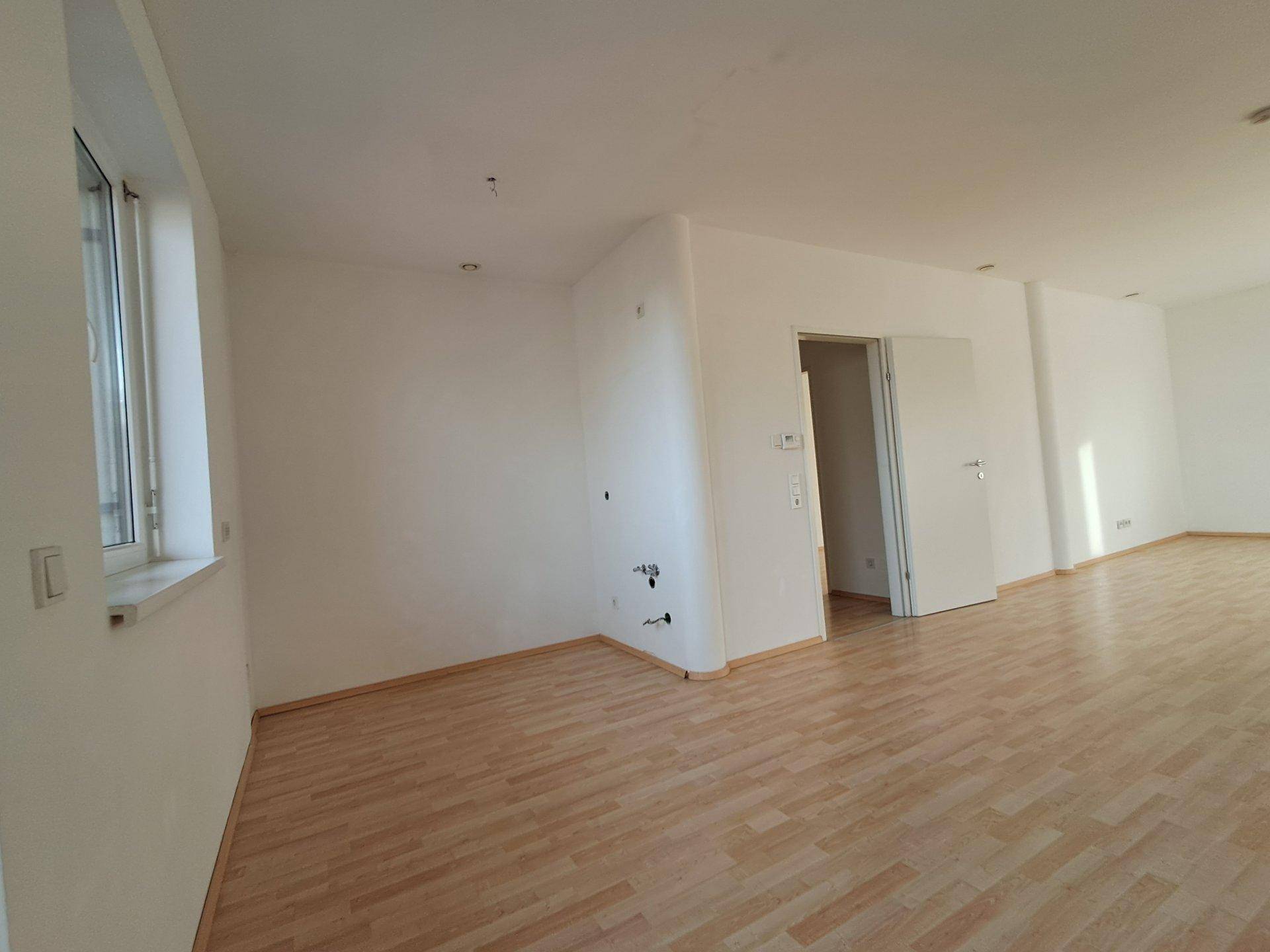 Geräumiger, heller Wohnbereich mit Laminatboden und Anschlüssen für eine zukünftige Küche.