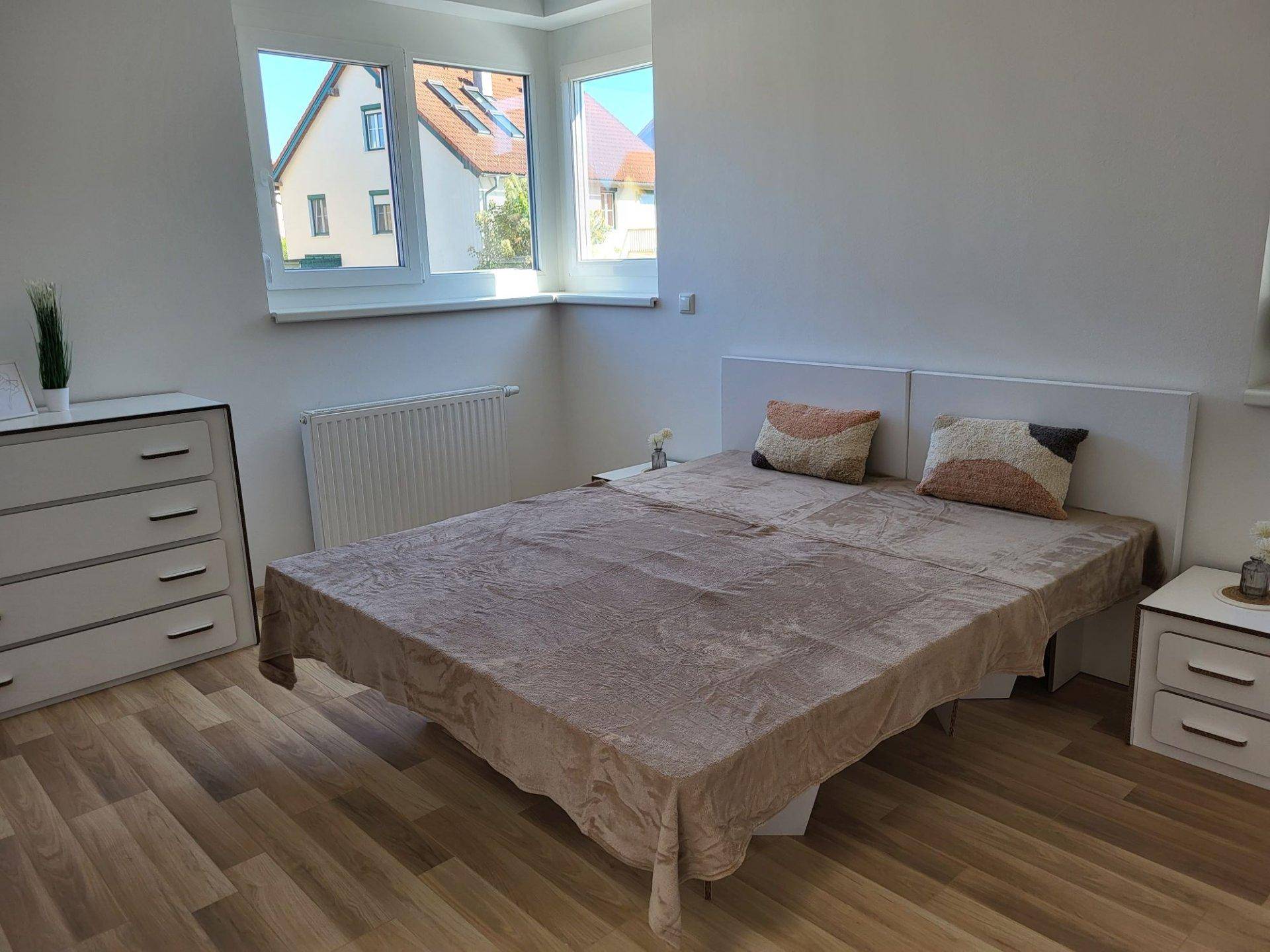 Helles Schlafzimmer mit Laminatboden, großem Fenster und Blick auf die Umgebung.