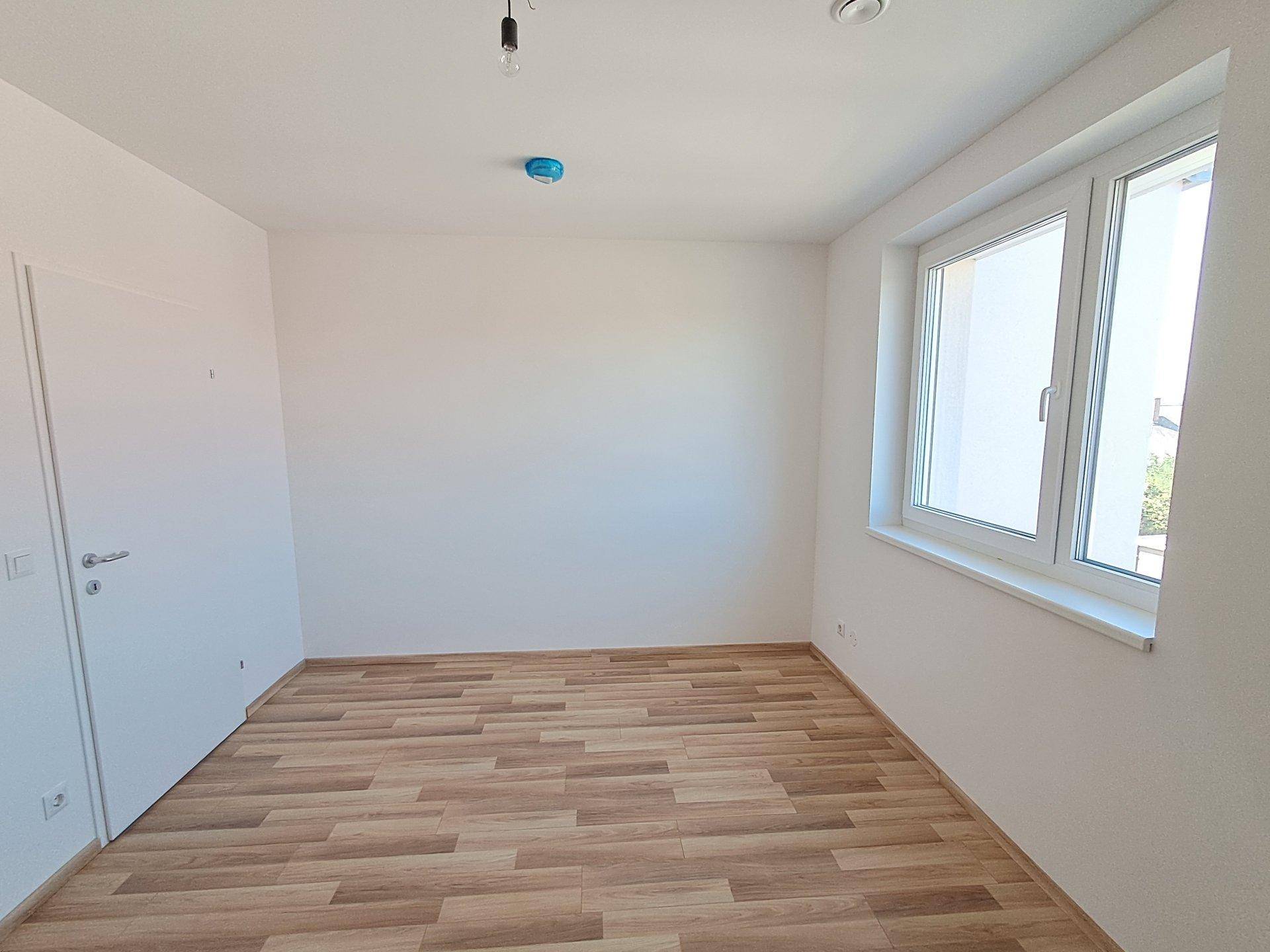 Helles, leeres Schlafzimmer mit Laminatboden und einem großen Fenster mit Ausblick.