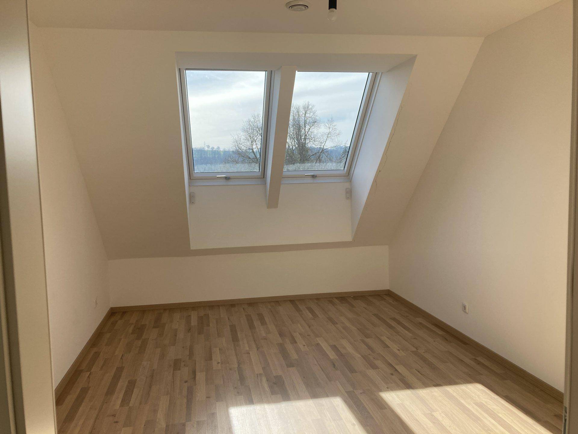 Schlafzimmer mit Laminatboden, Dachschrägen und zwei großen Dachfenstern für viel Licht.