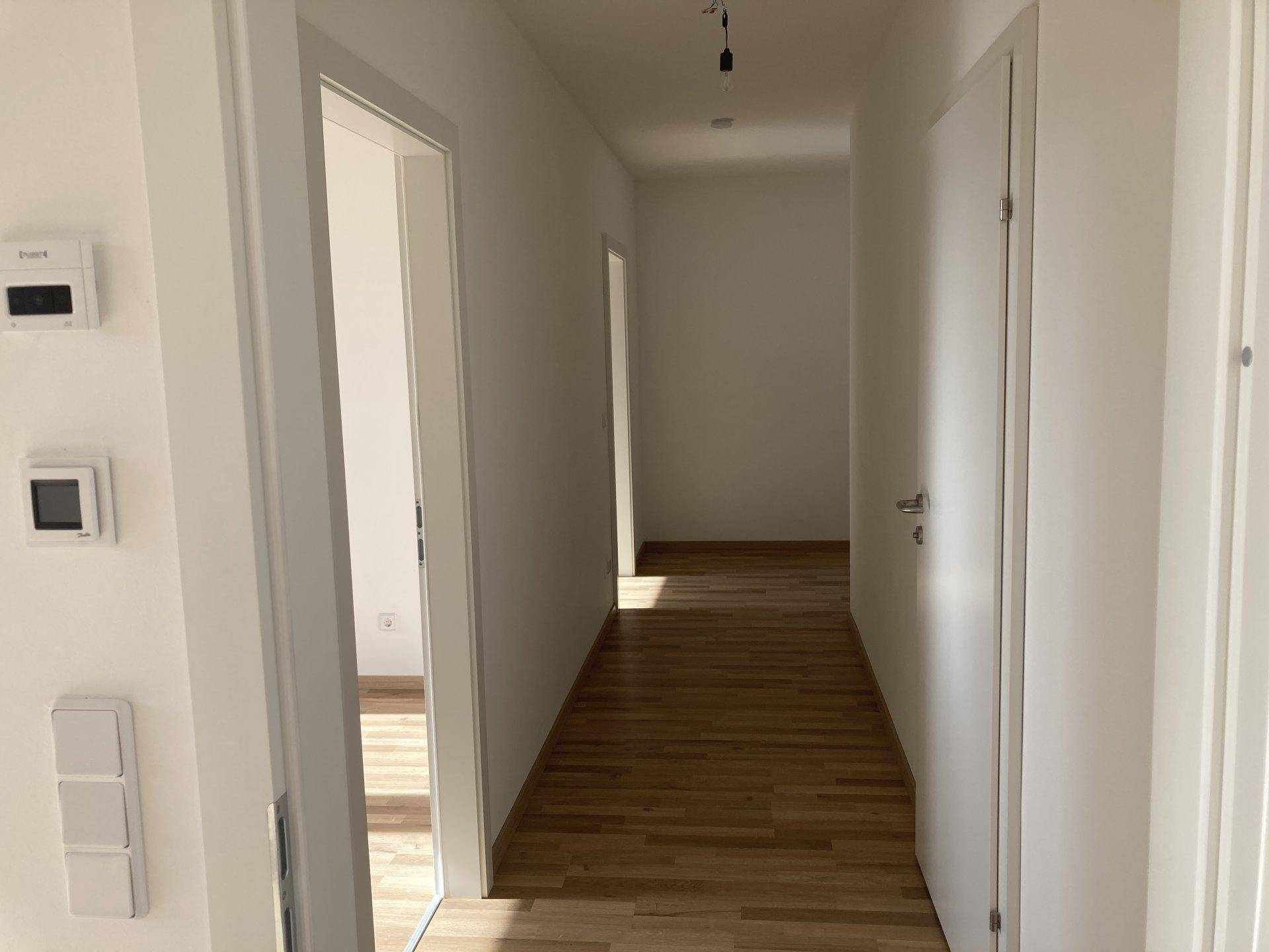 Heller Flur mit Laminatboden und weißen Wänden, der zu den angrenzenden Räumen führt.
