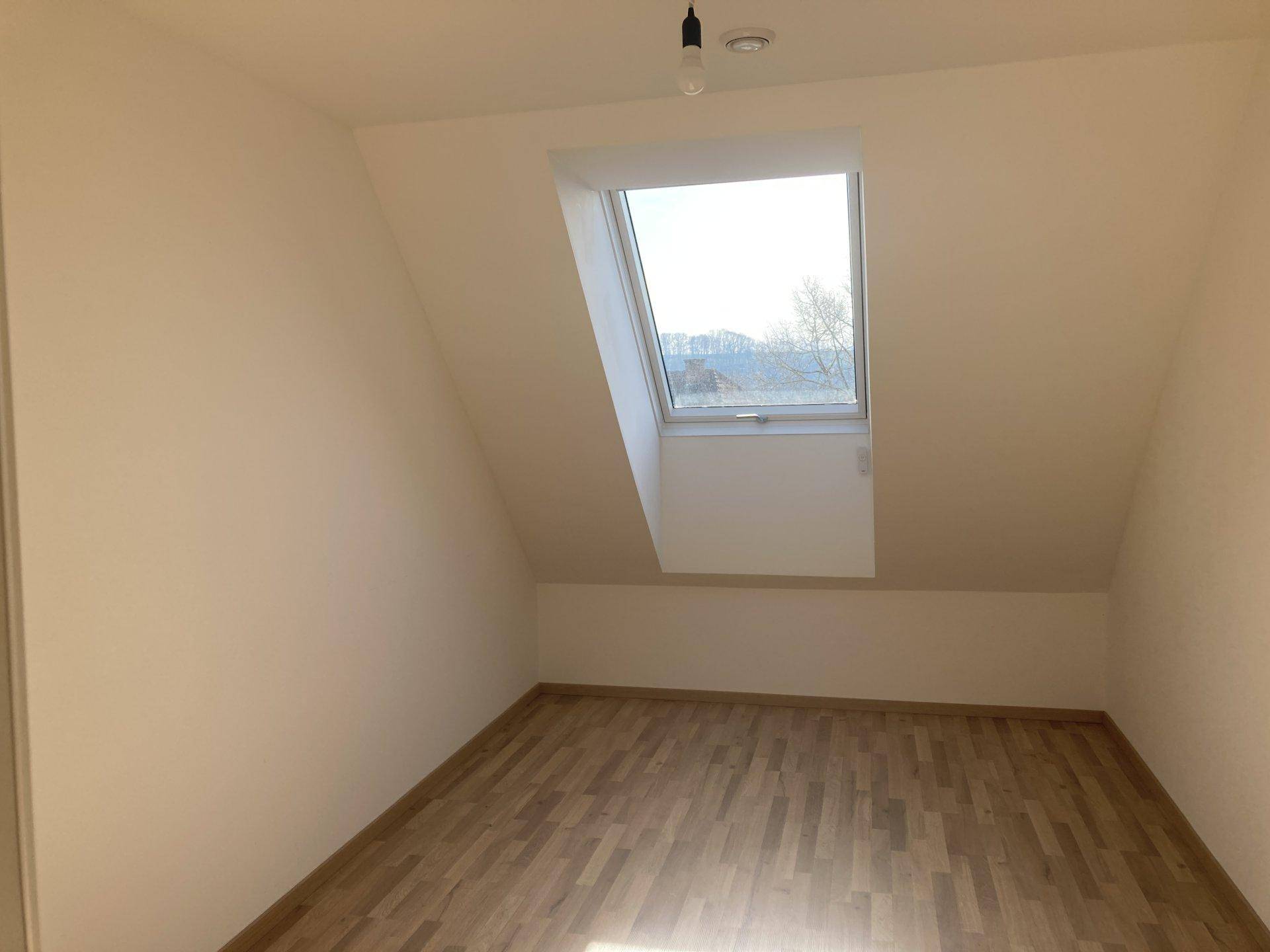 Helles Schlafzimmer mit Laminatboden, Dachschräge und einem großen Dachfenster.