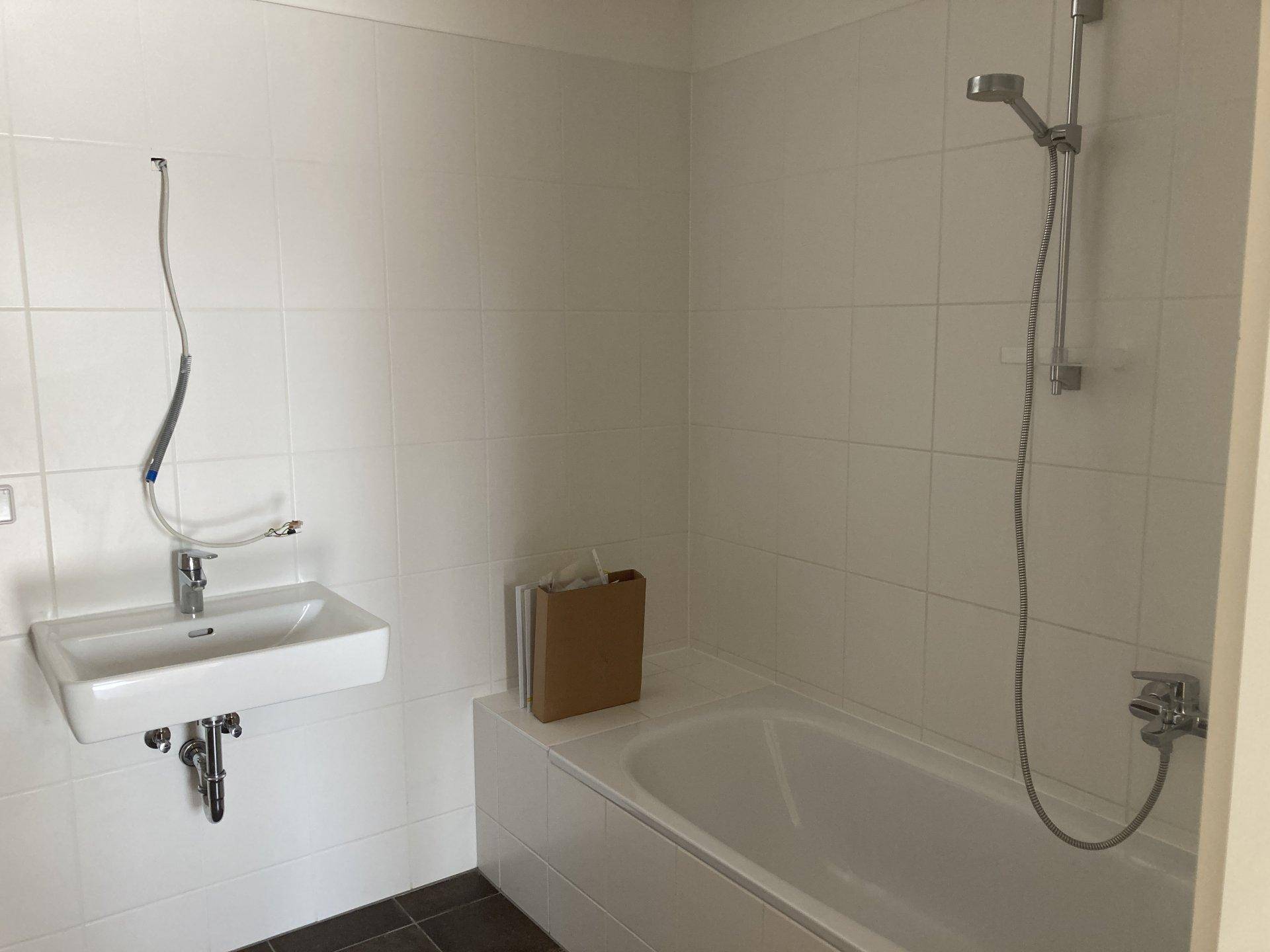 Helles Badezimmer mit Badewanne, Duschkopf, Waschbecken und weißen Wandfliesen.