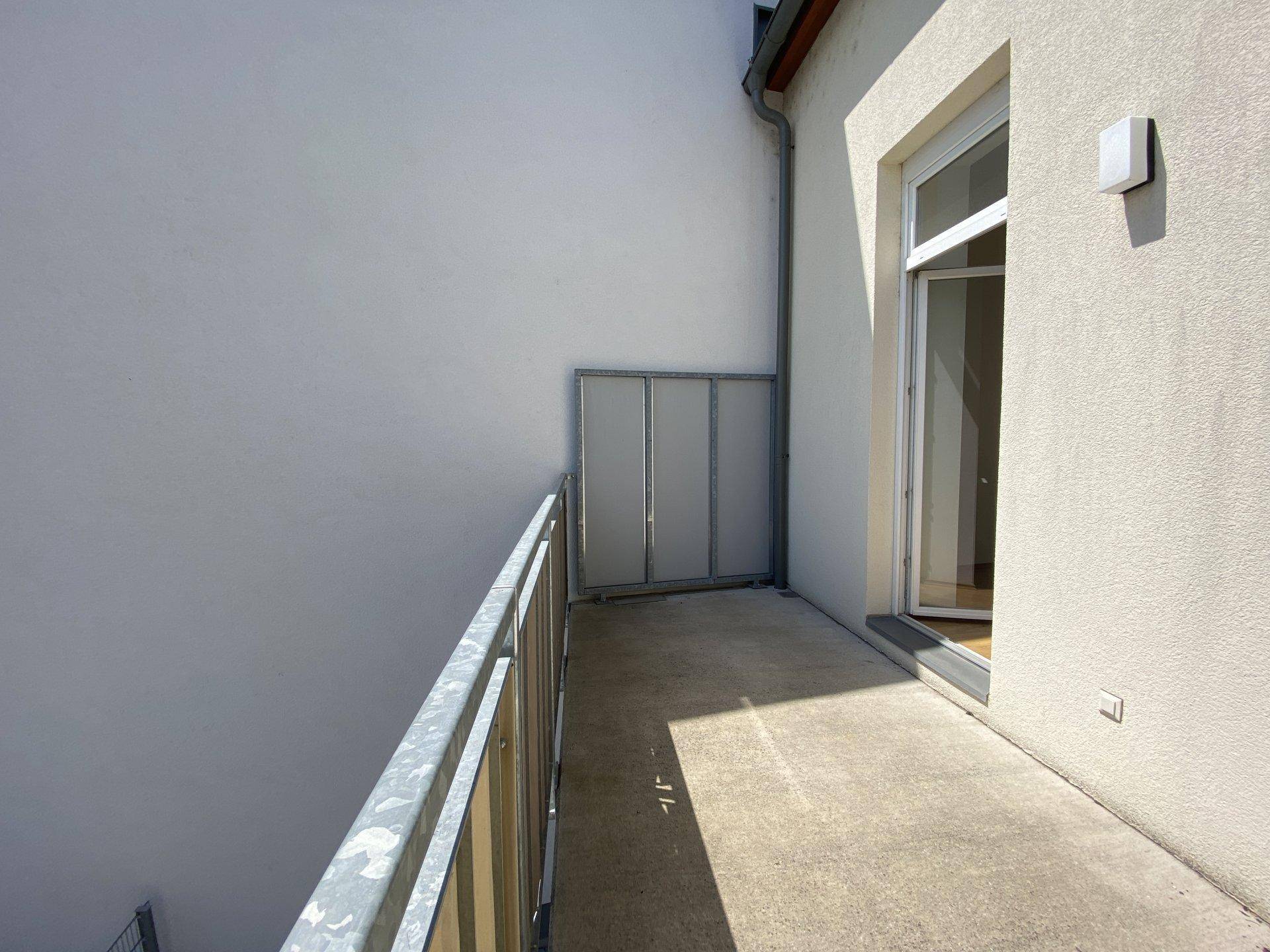Schmaler Balkon mit Metallgeländer und Zugang zu einem Innenraum, unter hellem Tageslicht.