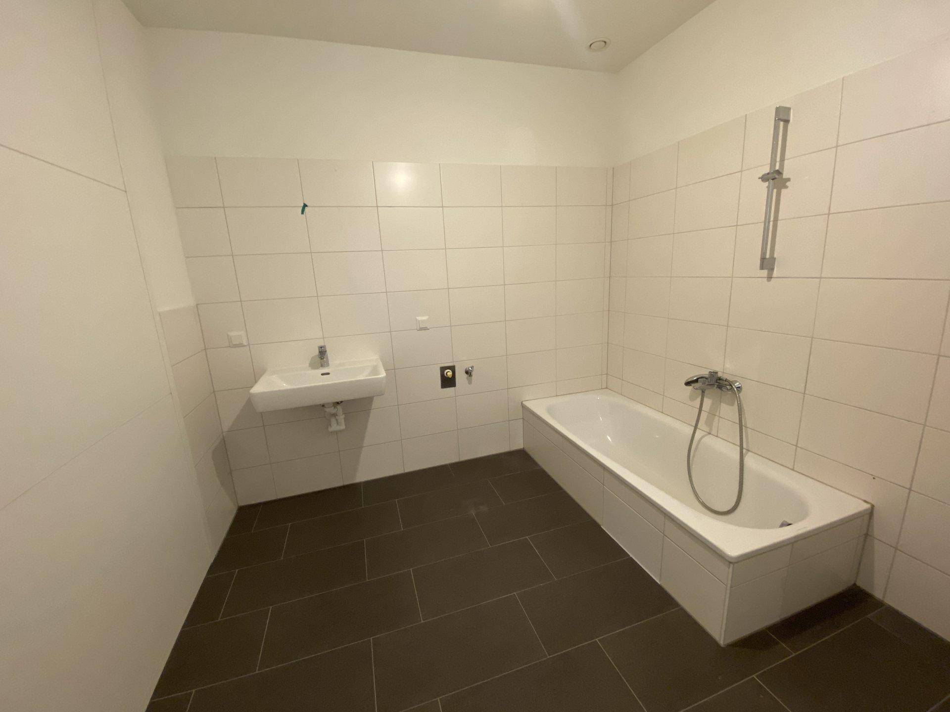 Modernes Badezimmer mit weißen Wandfliesen, dunklem Boden, Waschbecken und einer Badewanne.