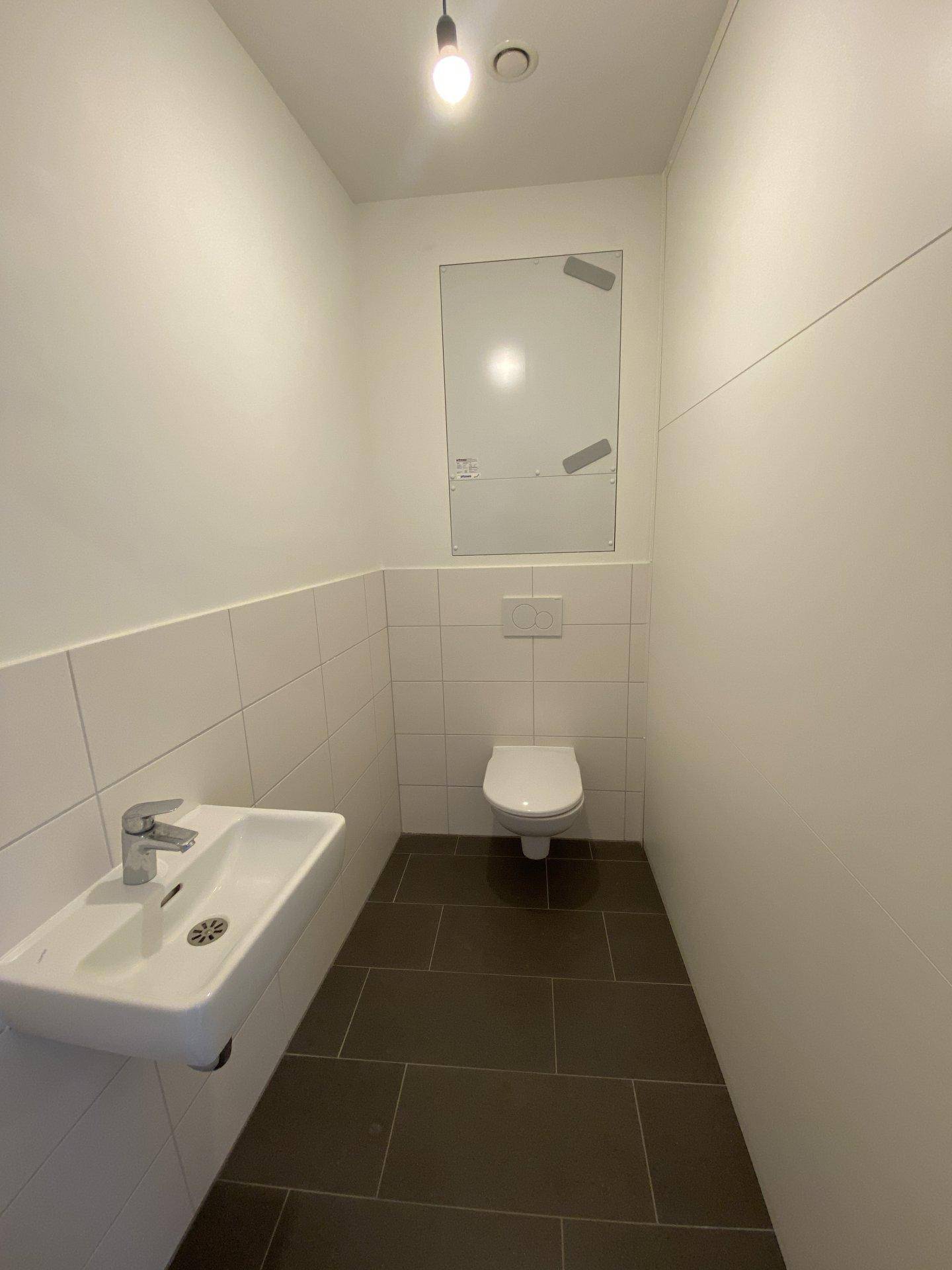 Kleines Gäste-WC mit wandhängender Toilette, Waschbecken und modernen Fliesen.