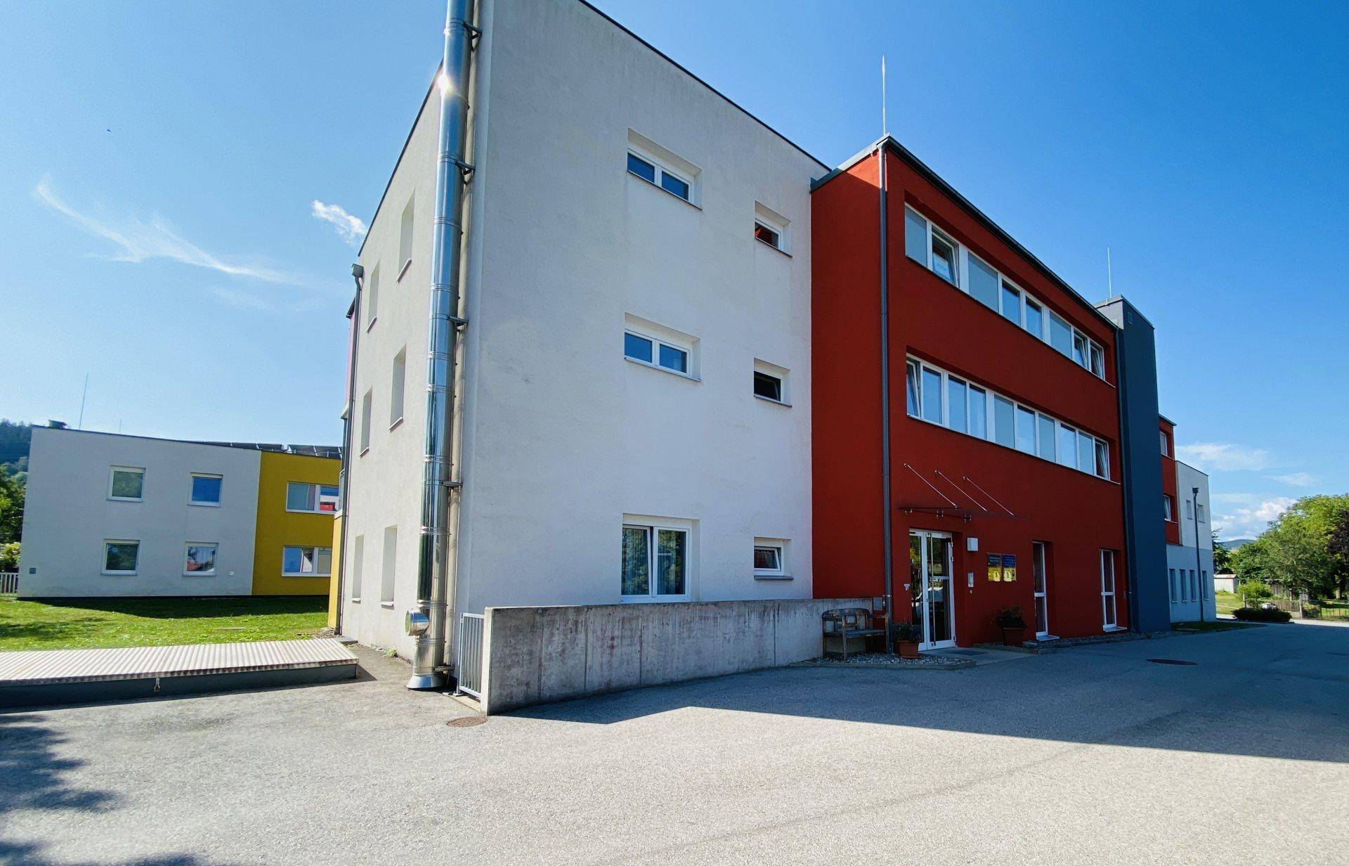 Seitenansicht eines modernen Gebäudes mit roter und weißer Fassade sowie vielen Fenstern.