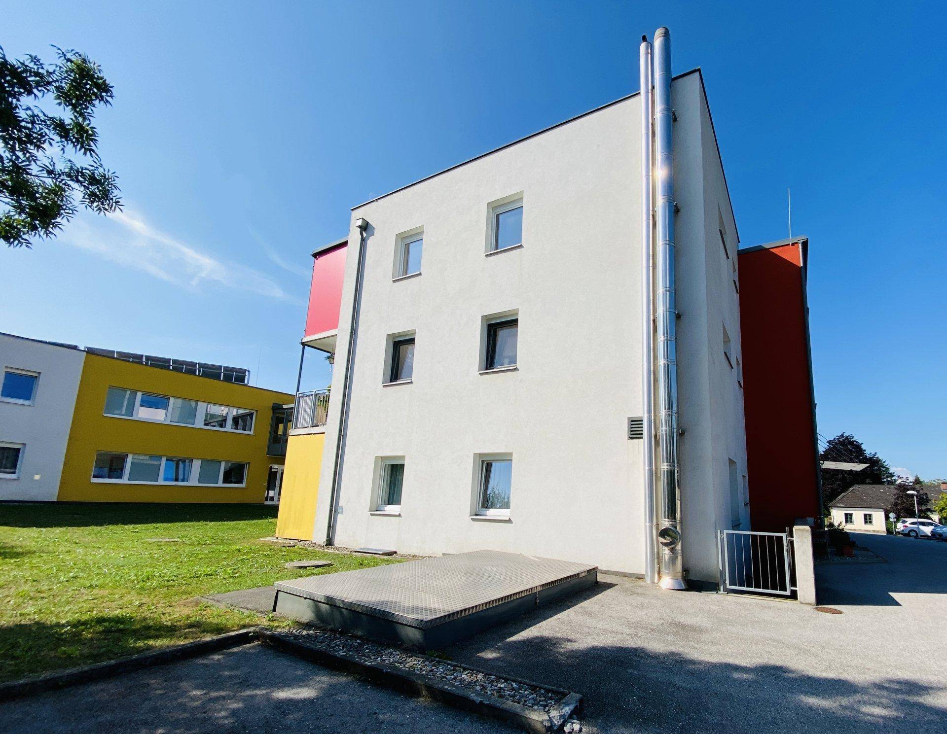 Modernes Gebäude mit weißer Fassade und auffälligem Metallkamin unter klarem blauem Himmel.