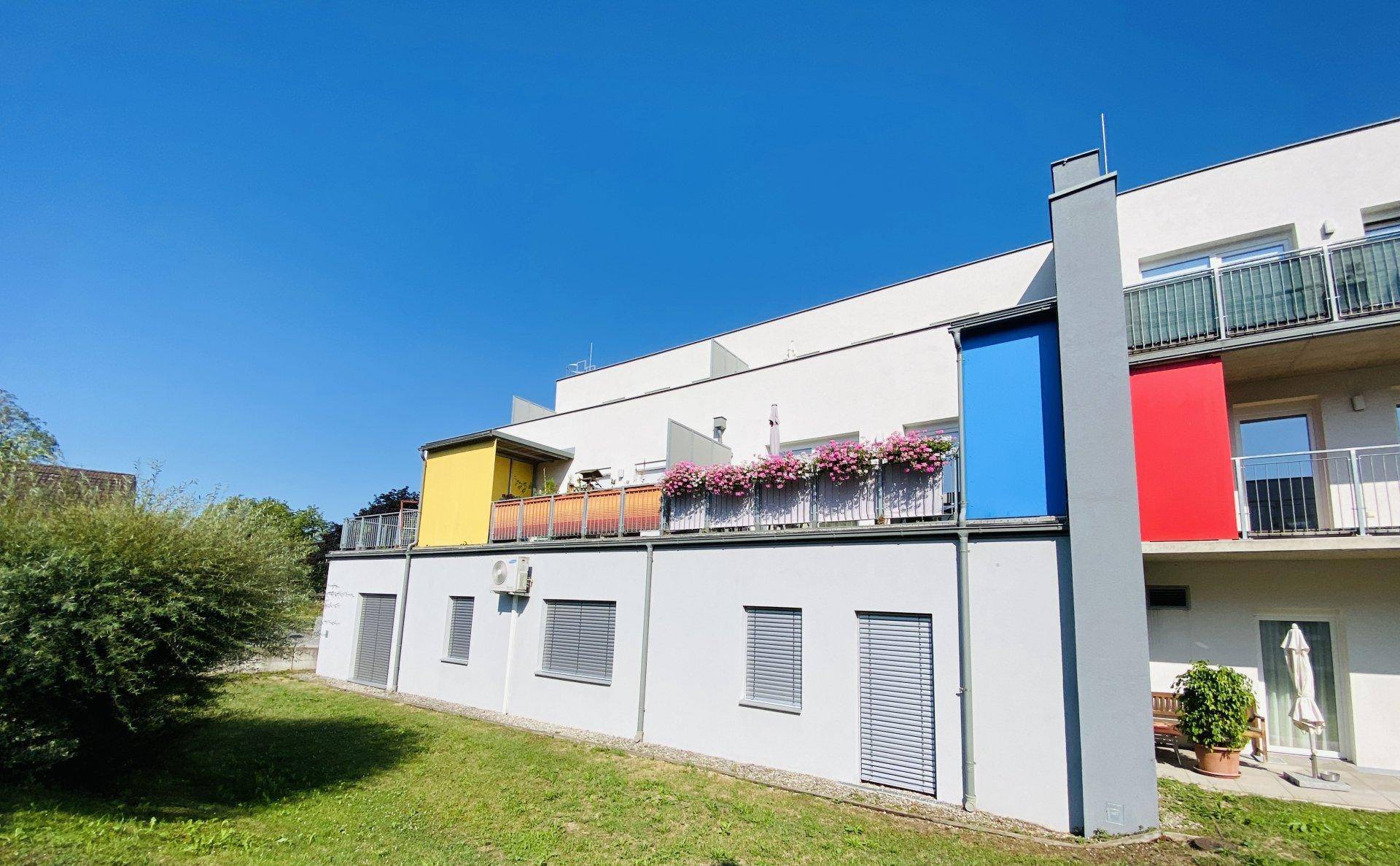 Modernes Gebäude mit farbigen Balkonen und einer kleinen Grünfläche an einem sonnigen Tag.