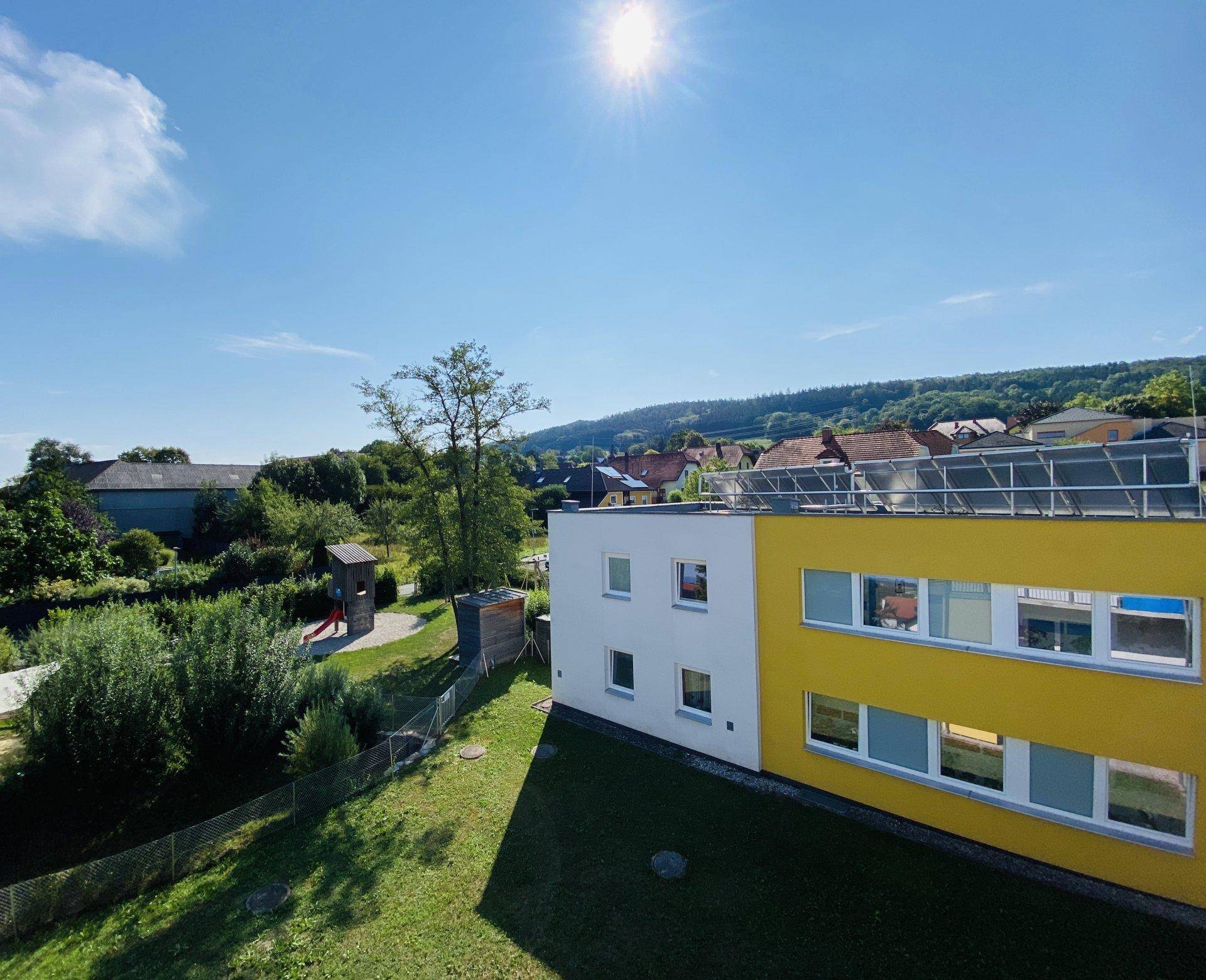 Luftaufnahme eines modernen Gebäudes mit Spielplatz und weitem Blick über die grüne Landschaft.