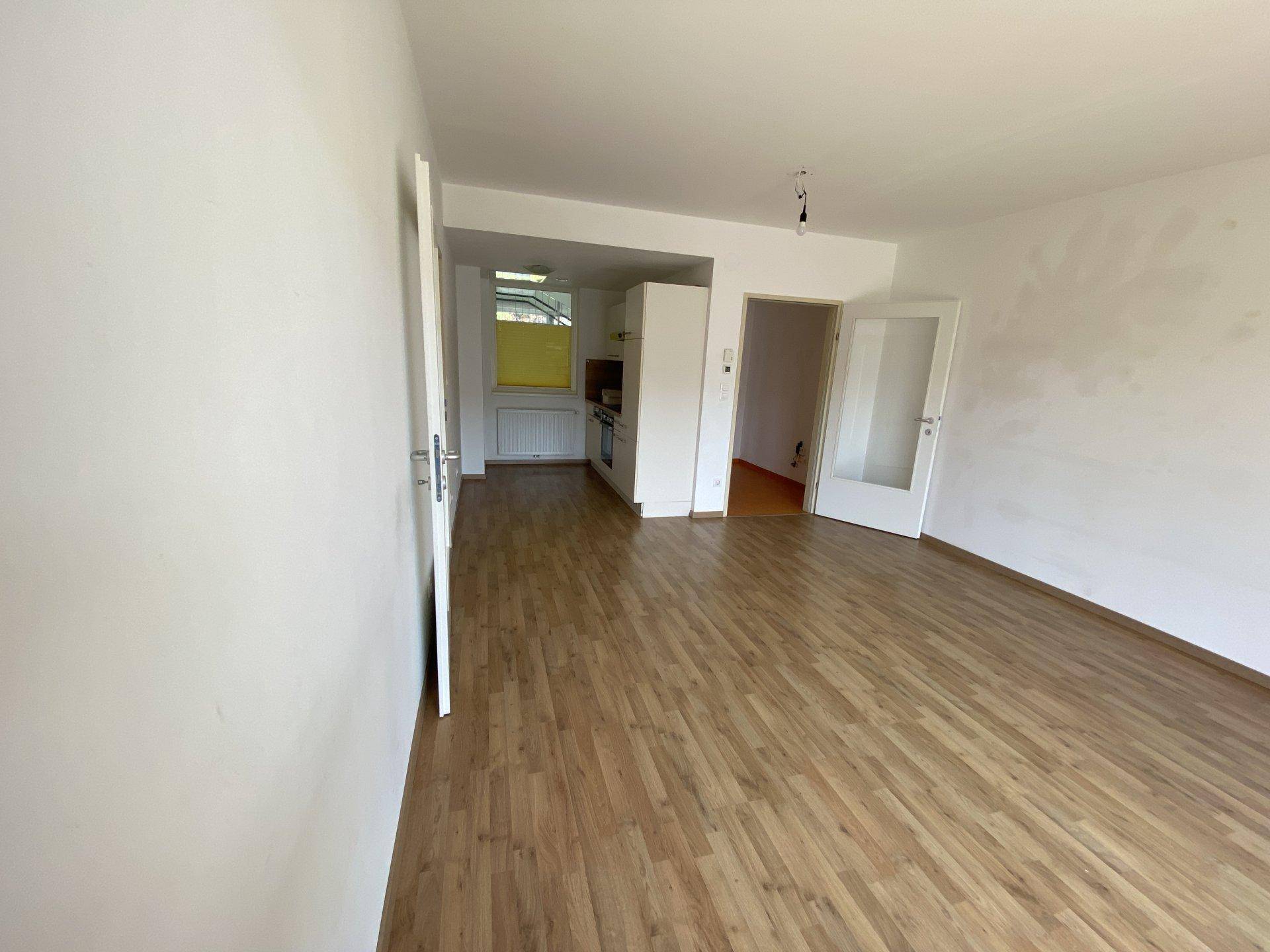 Geräumiges Wohnzimmer mit Laminatboden und Blick auf den angrenzenden Küchenbereich.