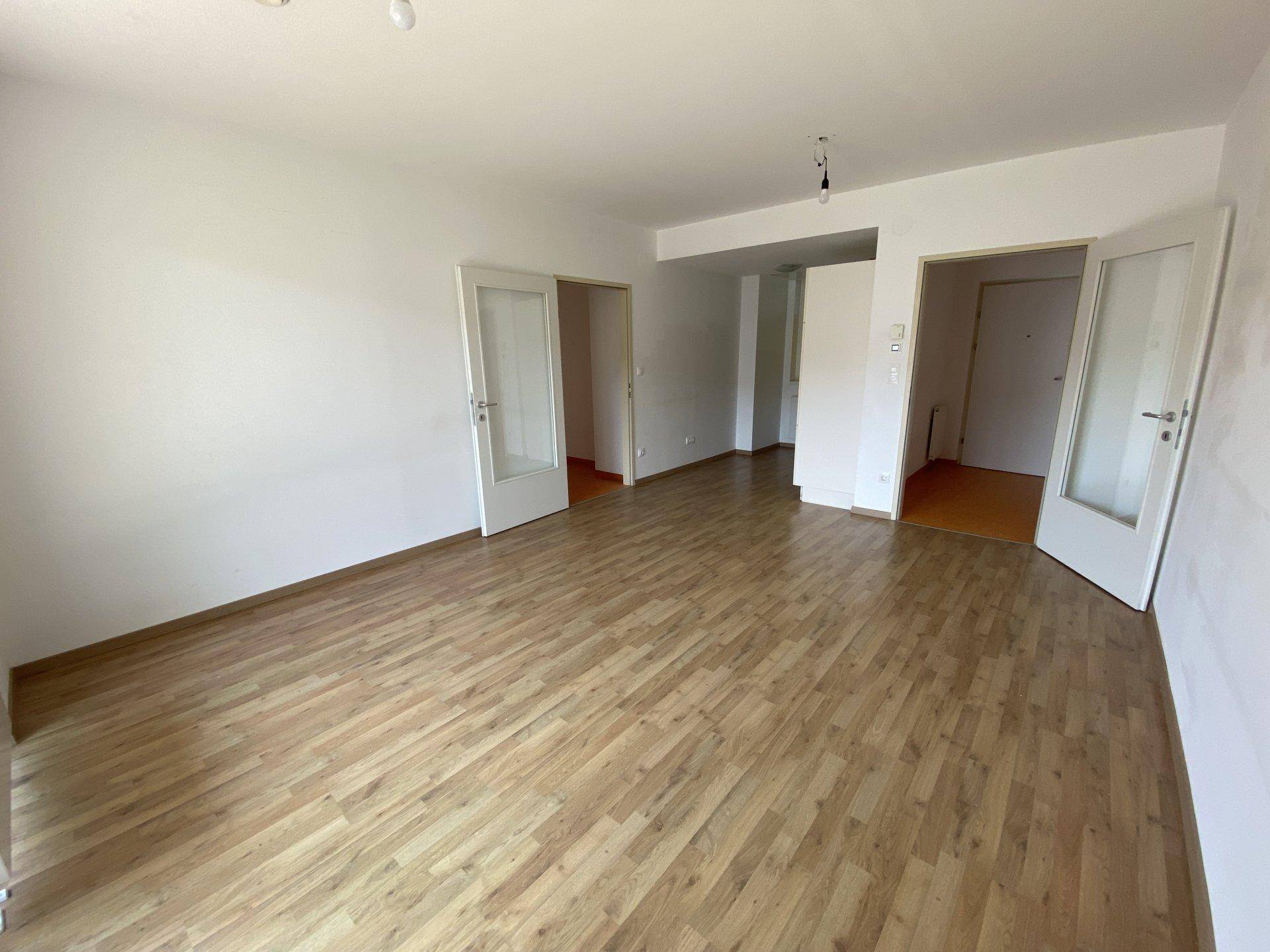 Helles Wohnzimmer mit Laminatboden und weißen Wänden, bereit zur individuellen Gestaltung.