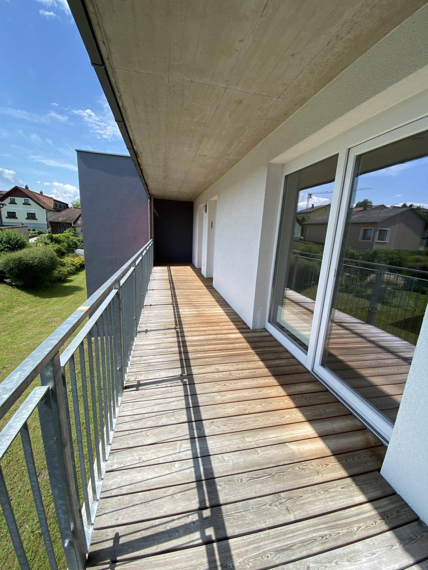 Langer Balkon mit Holzboden und Metallgeländer, bietet einen weiten Blick ins Grüne.