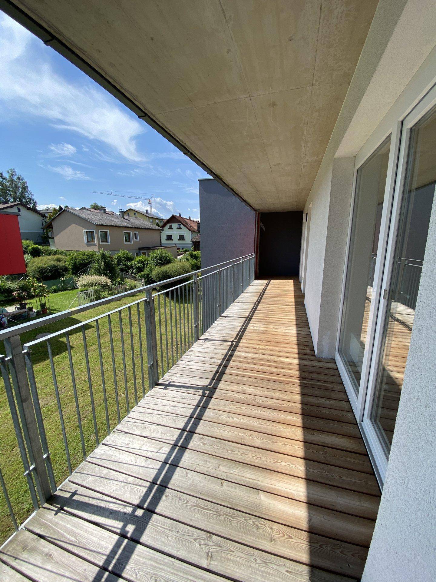 Geräumiger Balkon mit Holzdielen und Blick auf die umliegende Wohngegend und Natur.