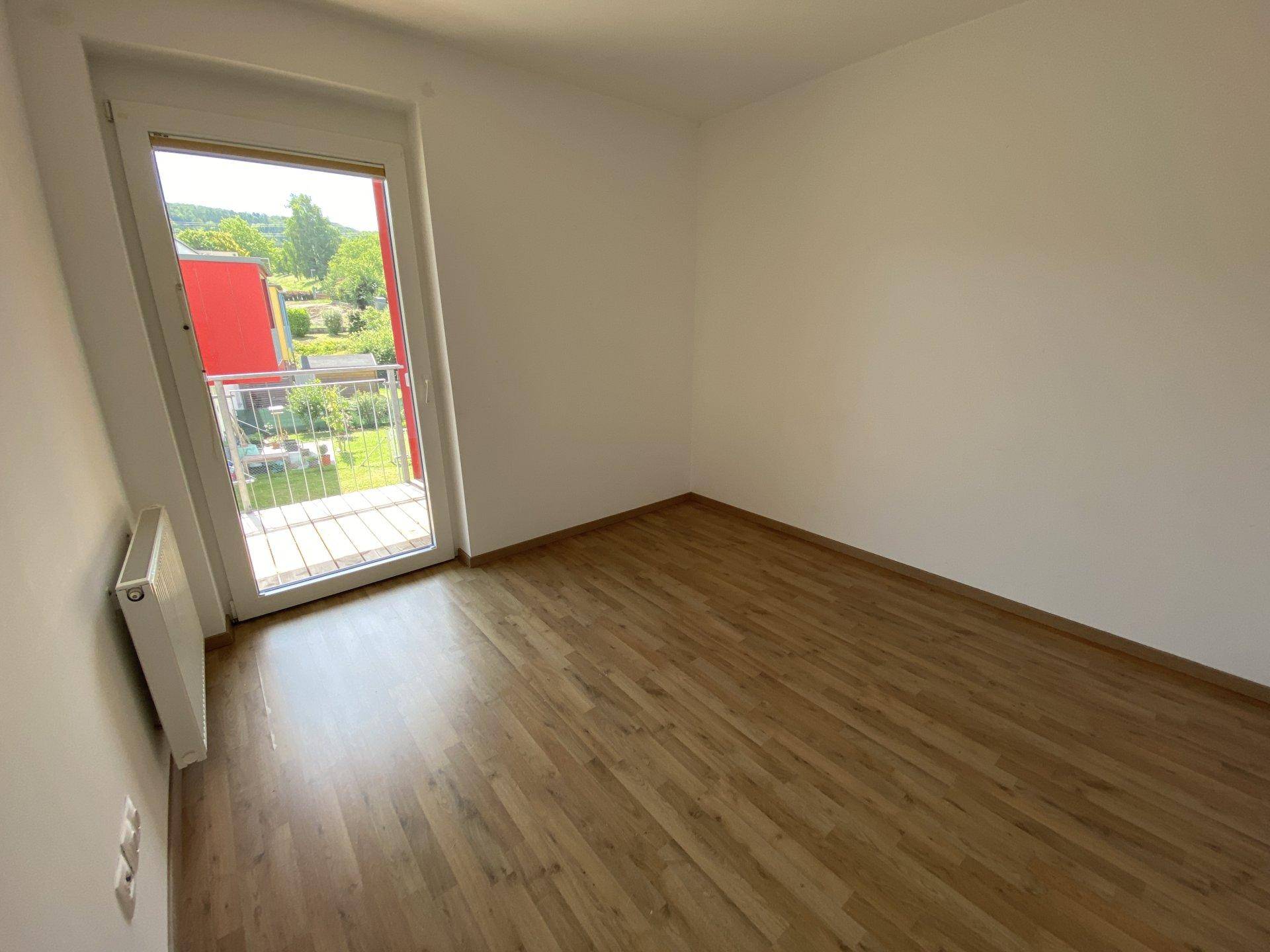 Schlafzimmer mit Laminatboden und Zugang zu einem Balkon, bietet viel natürliches Licht.