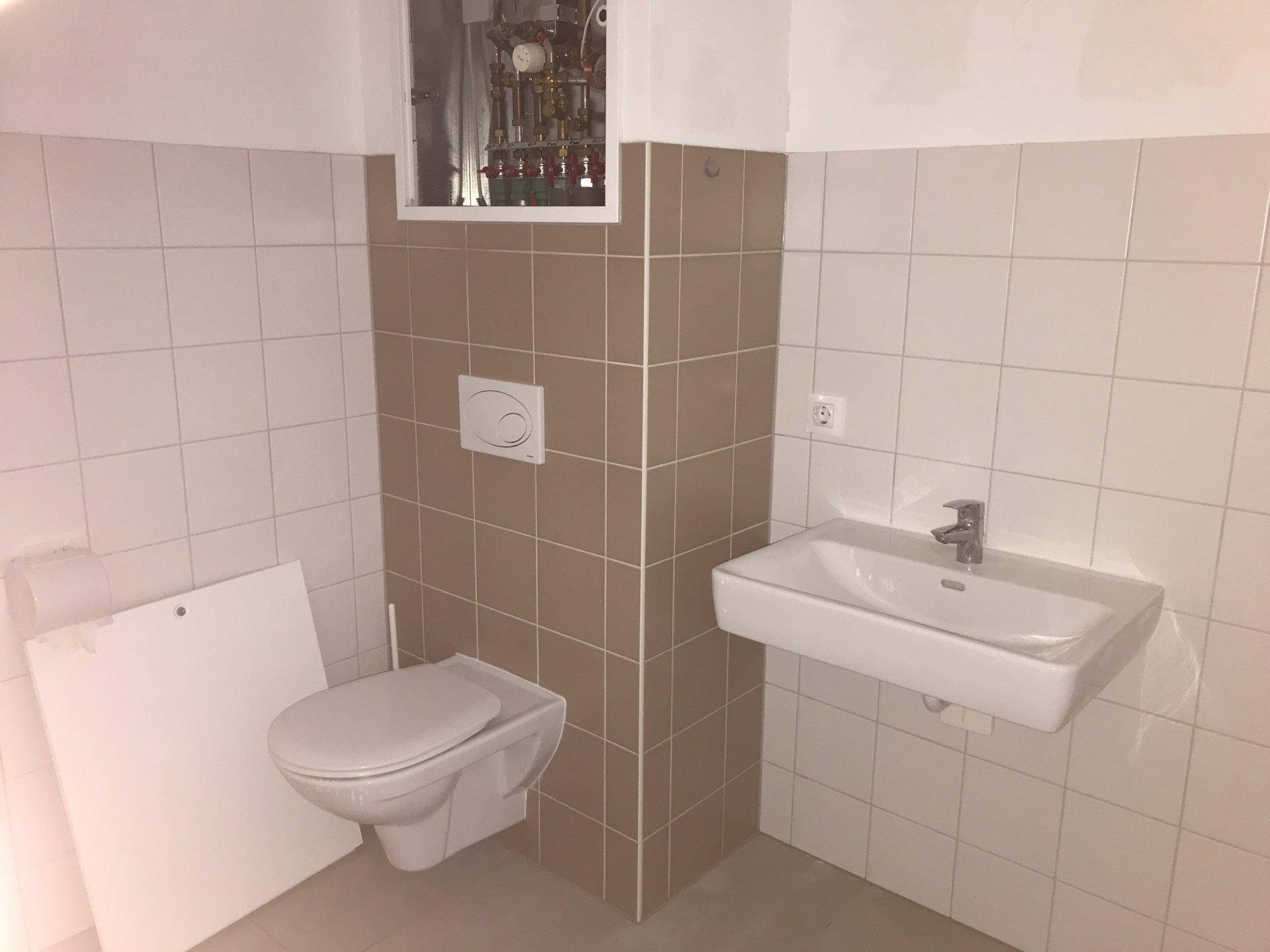 Modernes Gäste-WC mit Wand-WC und Waschbecken, gefliest in Weiß und Braun.