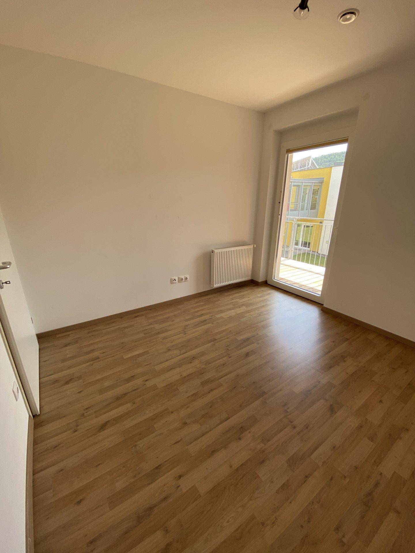 Helles Schlafzimmer mit Laminatboden und Balkonzugang, ideal für erholsame Nächte.