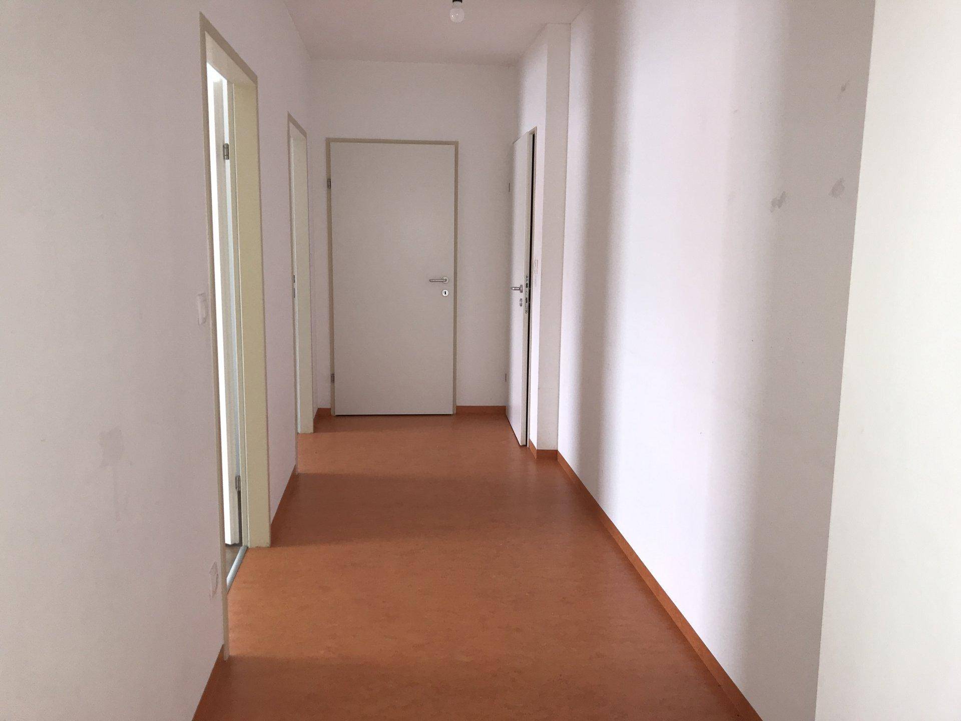 Heller Flur mit braunem Linoleumboden und weißen Wänden, verbindet die verschiedenen Räume.