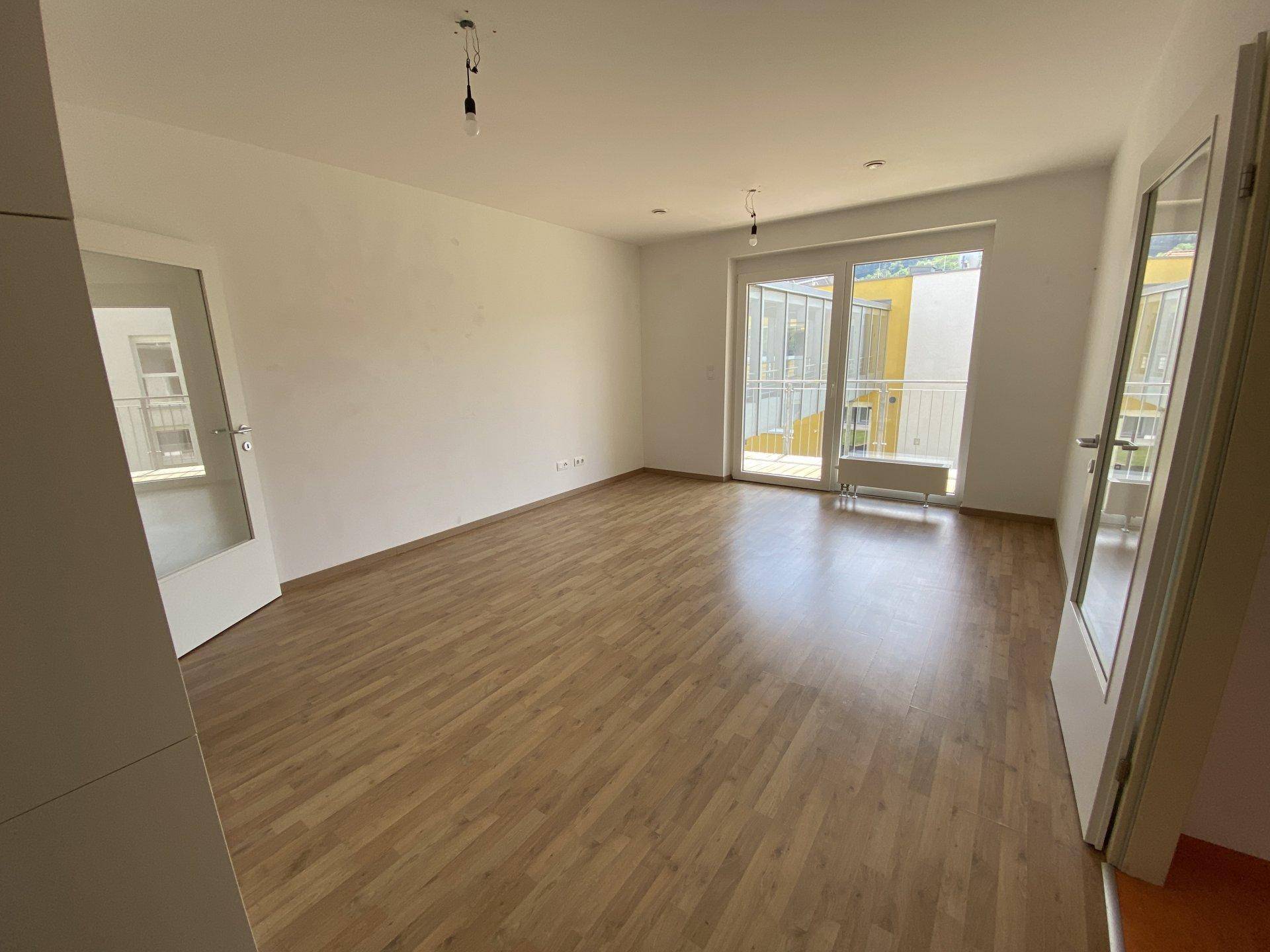 Helles Wohnzimmer mit Laminatboden und Zugang zu einem Balkon, bietet viel Tageslicht.