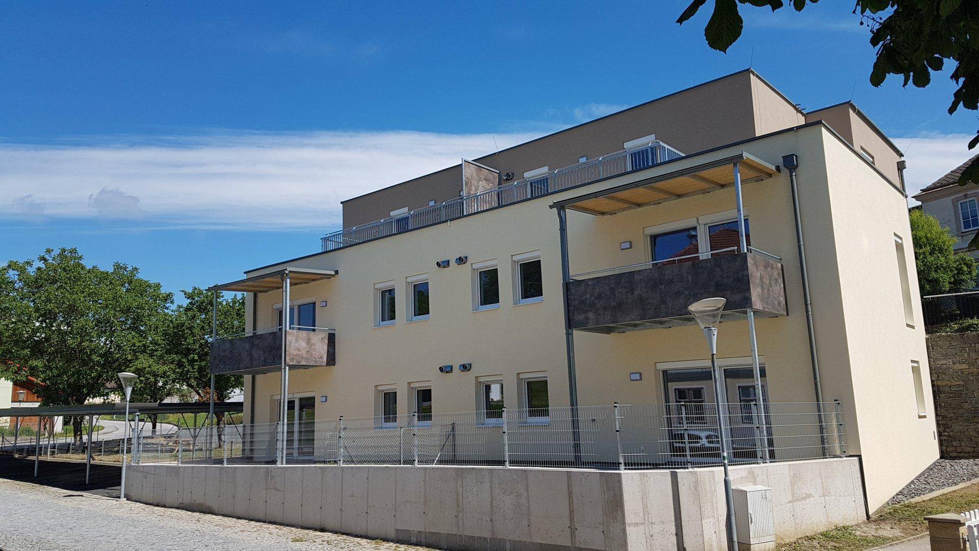 Rückansicht des Neubaus mit mehreren Balkonen und einem Carport im Vordergrund.