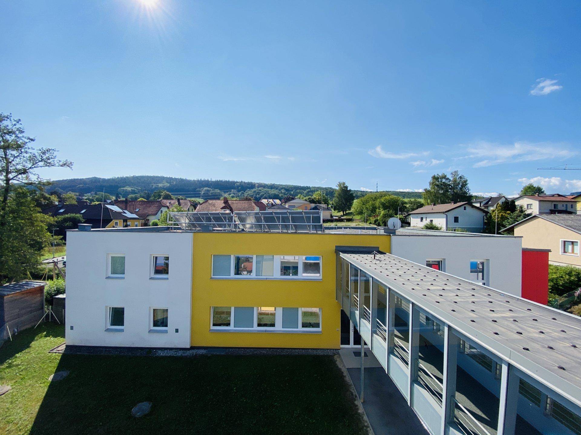 Weitläufige Ansicht eines modernen Gebäudes mit gelber Fassade und Verbindungsbrücke in ländlicher Umgebung.