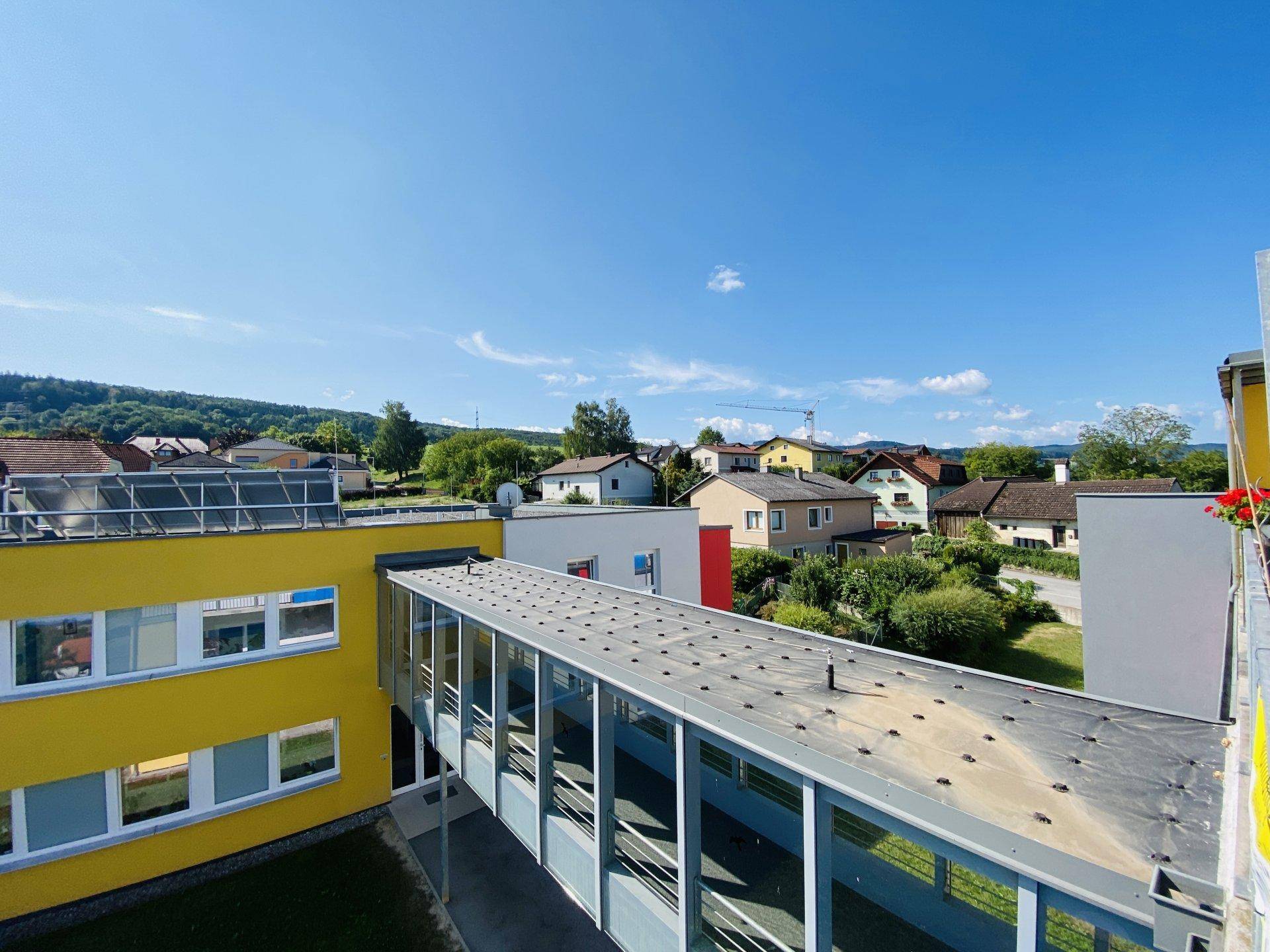 Luftaufnahme eines modernen Gebäudekomplexes mit Verbindungsbrücke und umliegender Wohnbebauung.