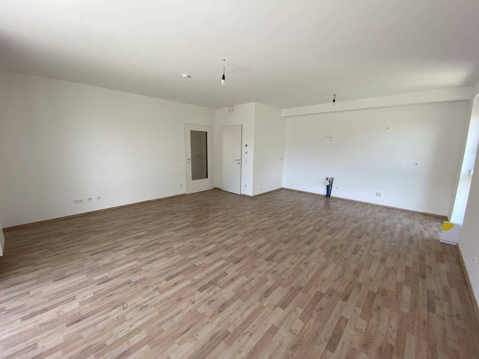 Geräumiger, leerer Wohnbereich mit Laminatboden und weißen Wänden, bereit für die Einrichtung.