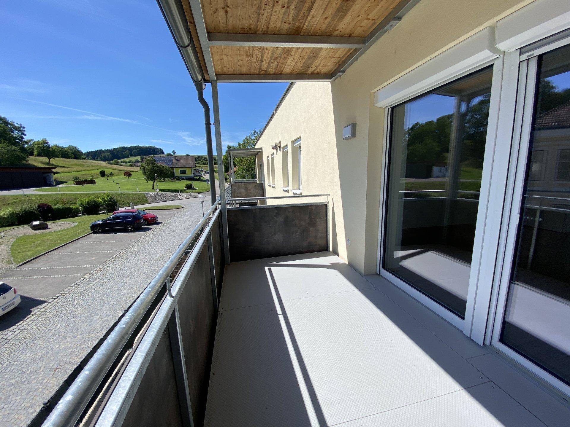Langer Balkon mit Holzdach und weitem Blick über die hügelige Landschaft und Parkplätze.