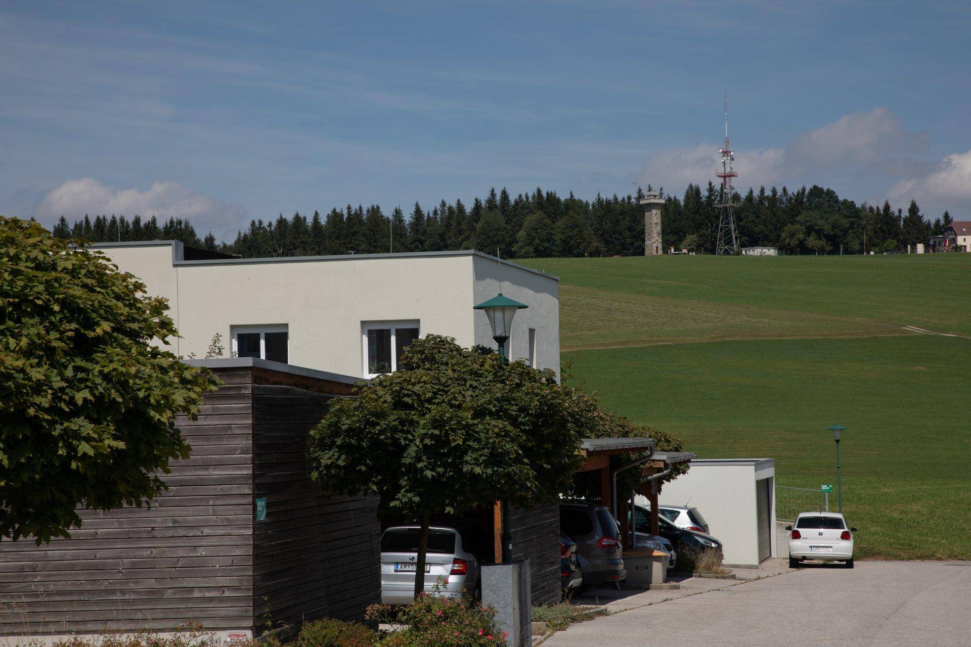 Wohngebäude mit Carports, umgeben von grünen Feldern und einem Aussichtsturm in der Ferne.