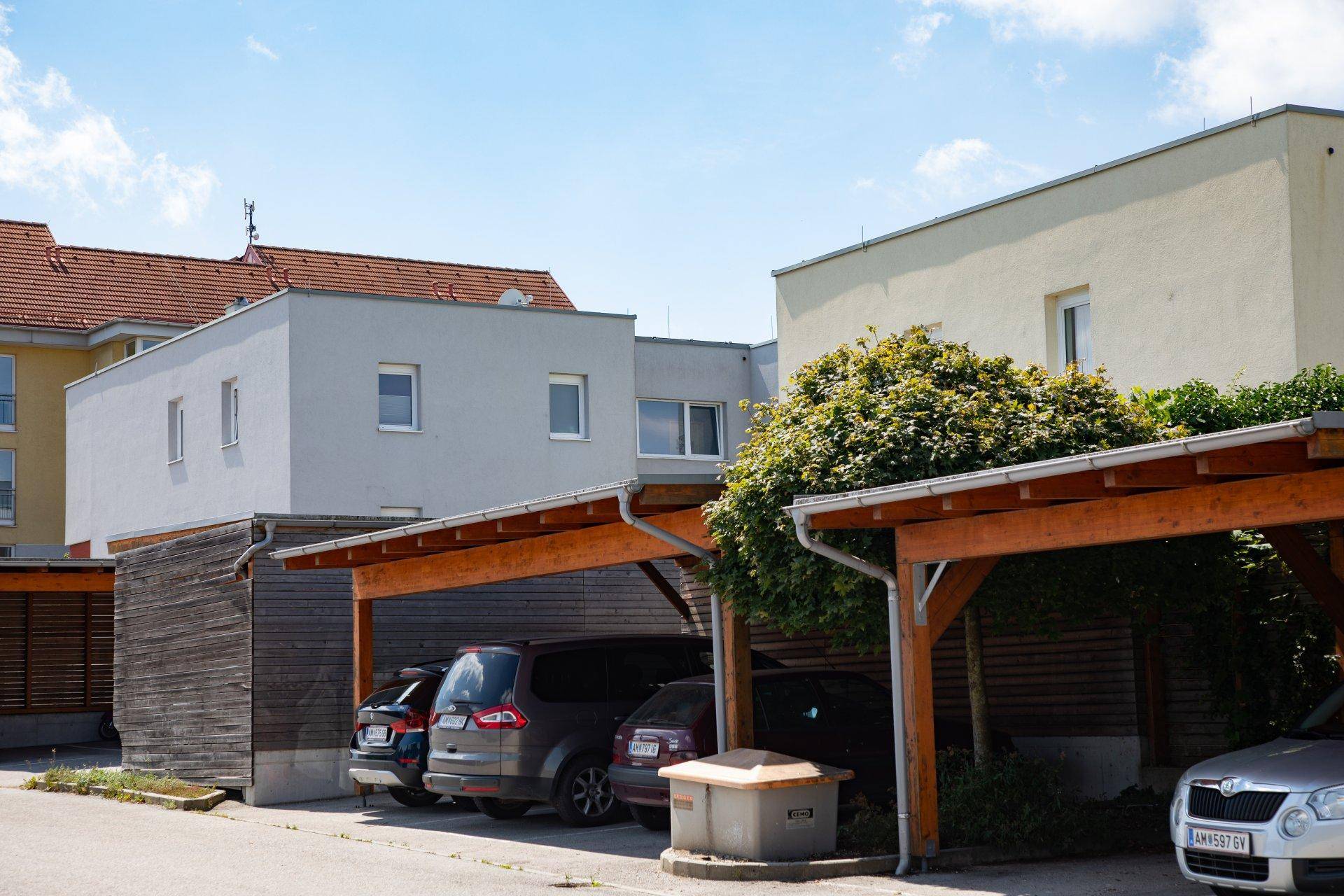 Reihe von Wohngebäuden mit Holzcarports und geparkten Autos an einem sonnigen Tag.