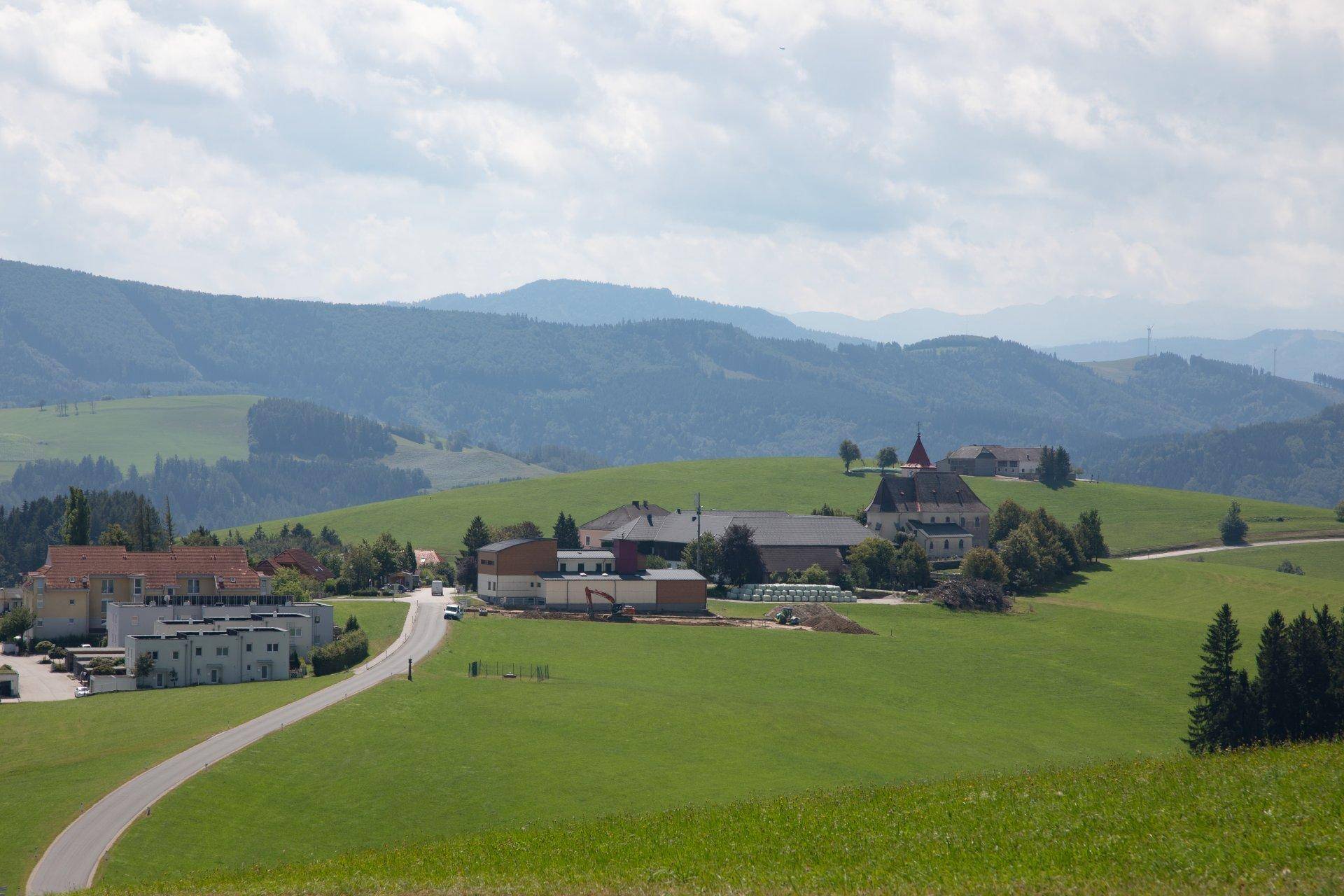 Malerisches Dorf eingebettet in eine weite, grüne Hügellandschaft unter blauem Himmel.