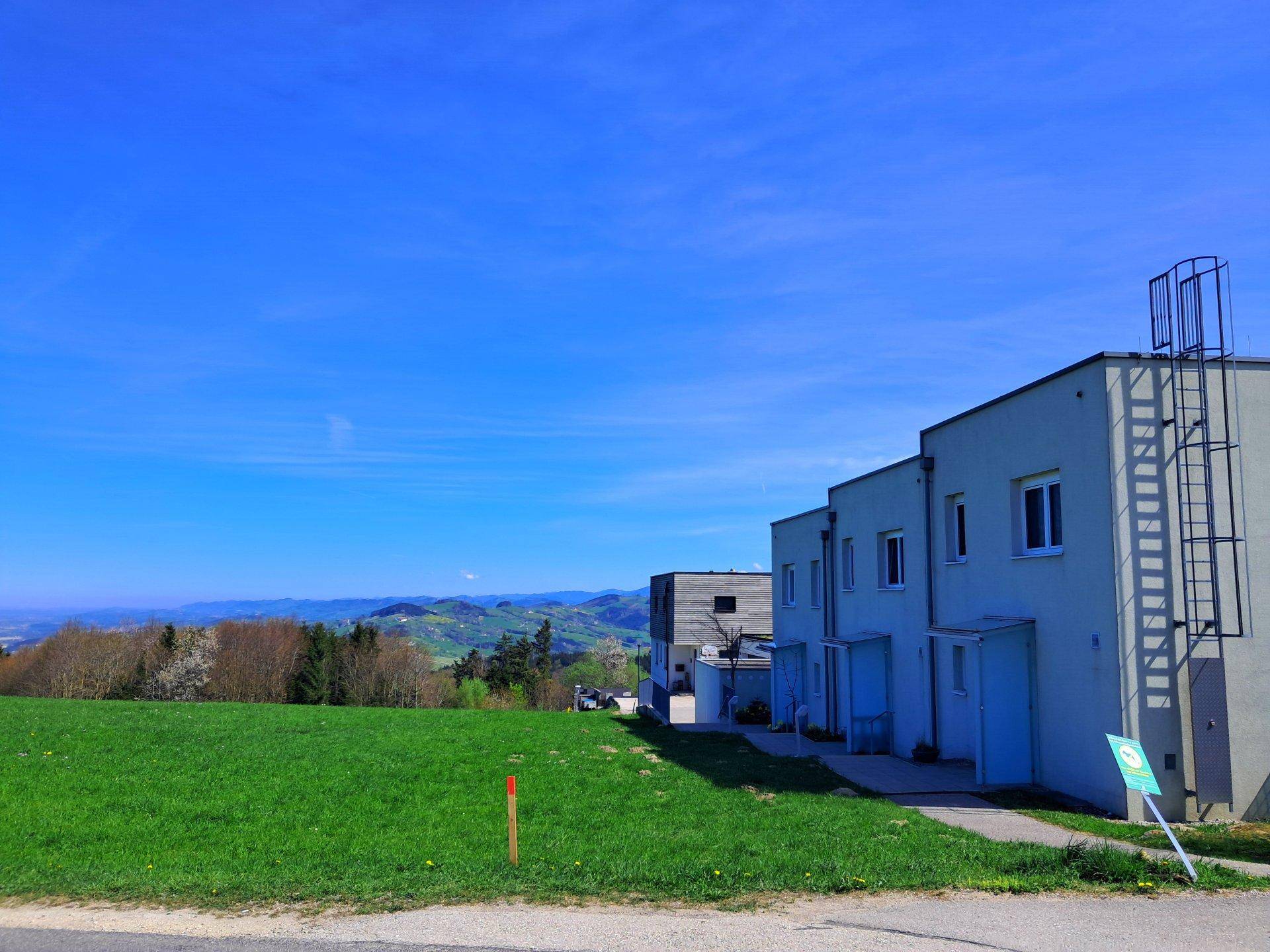 Moderne Wohngebäude mit weitem Blick über grüne Felder und hügelige Landschaft unter blauem Himmel.