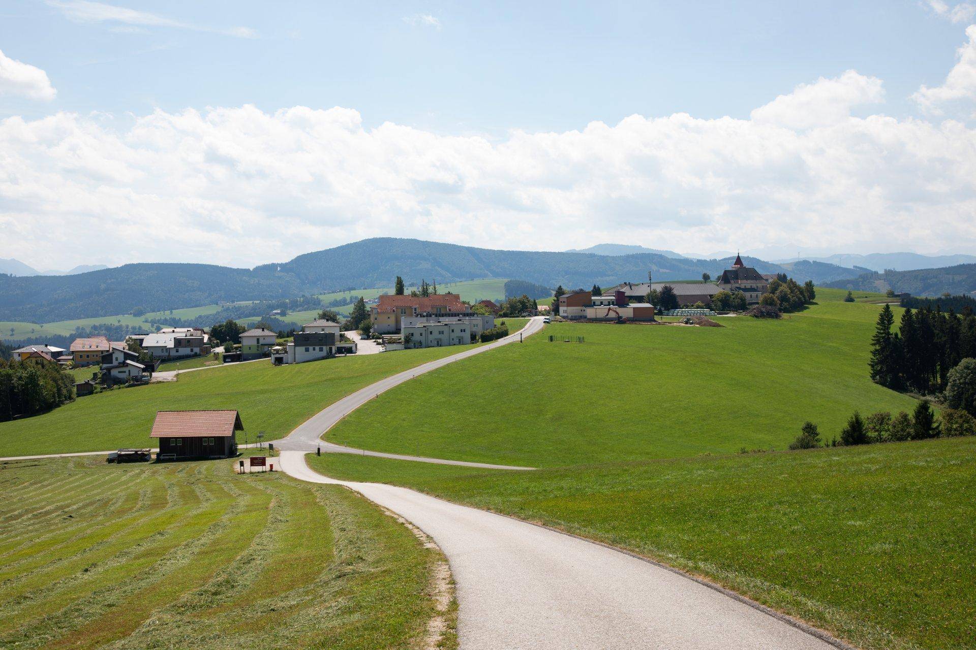 Weitläufige grüne Landschaft mit einem Dorf und einer Straße, die sich durch die Hügel schlängelt.