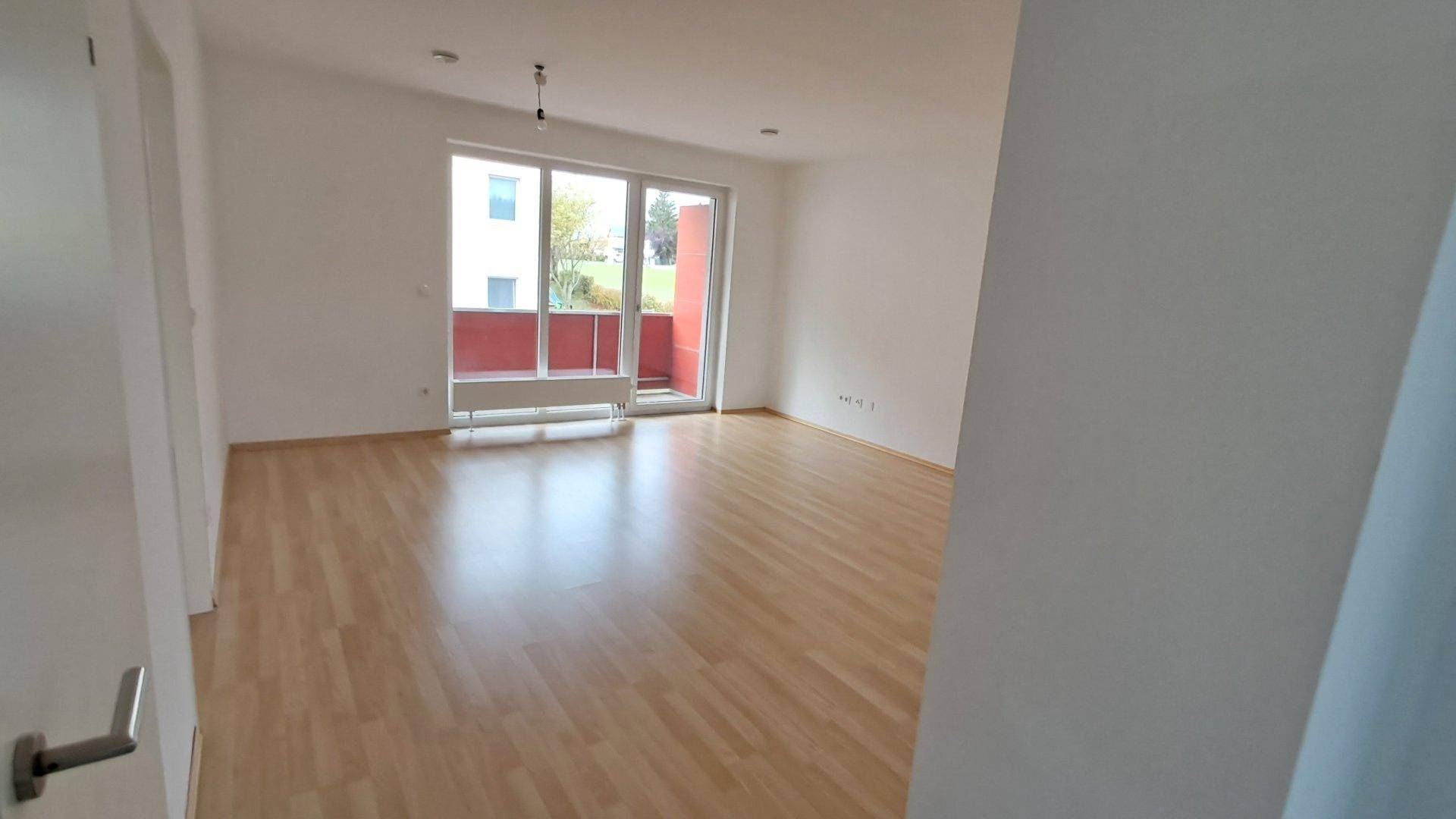 Helles Wohnzimmer mit Laminatboden und Zugang zu einem Balkon, bereit zur individuellen Gestaltung.