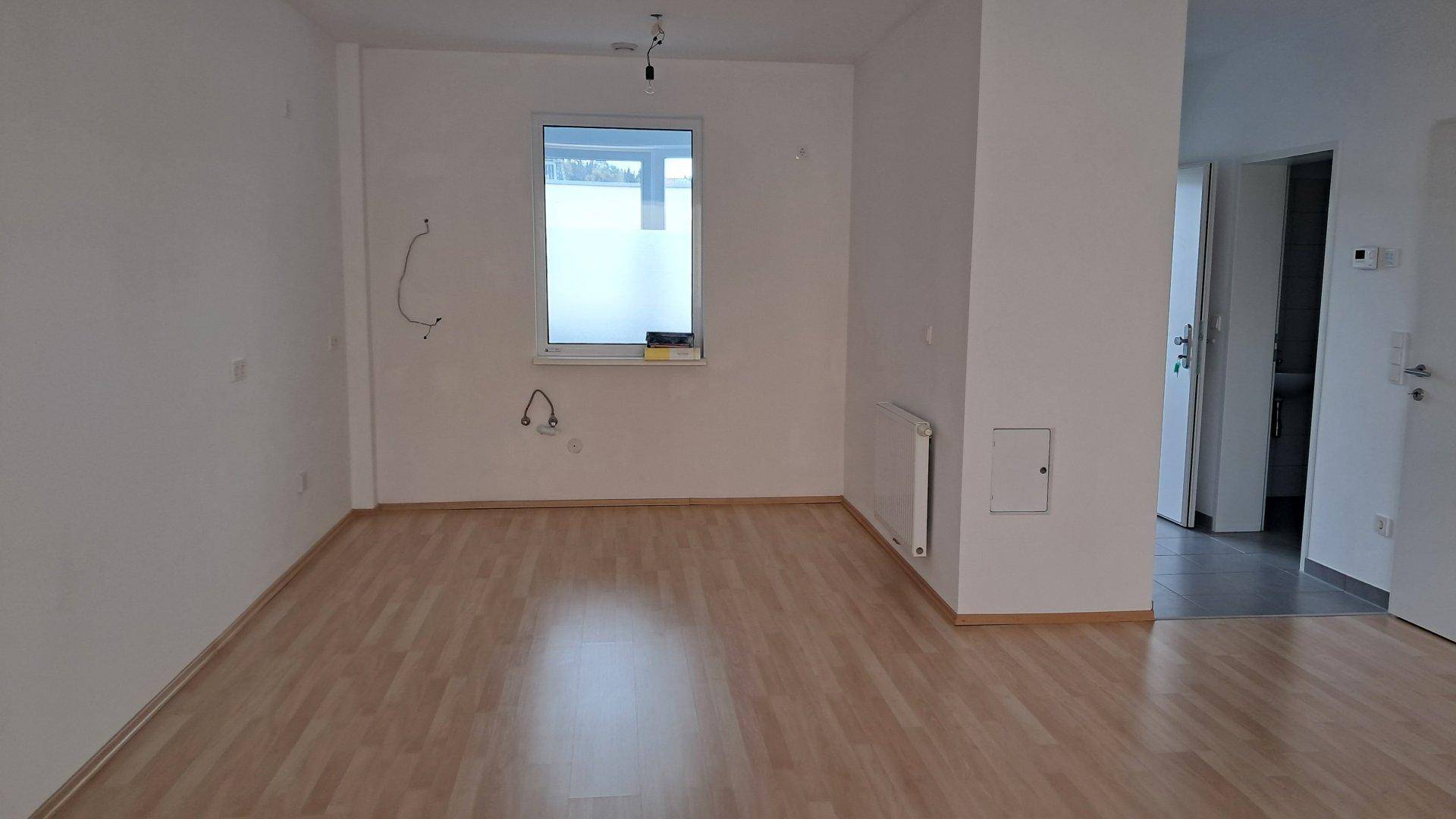 Leerer Raum mit Laminatboden und Fenster, vorbereitet für die Installation einer Küche.